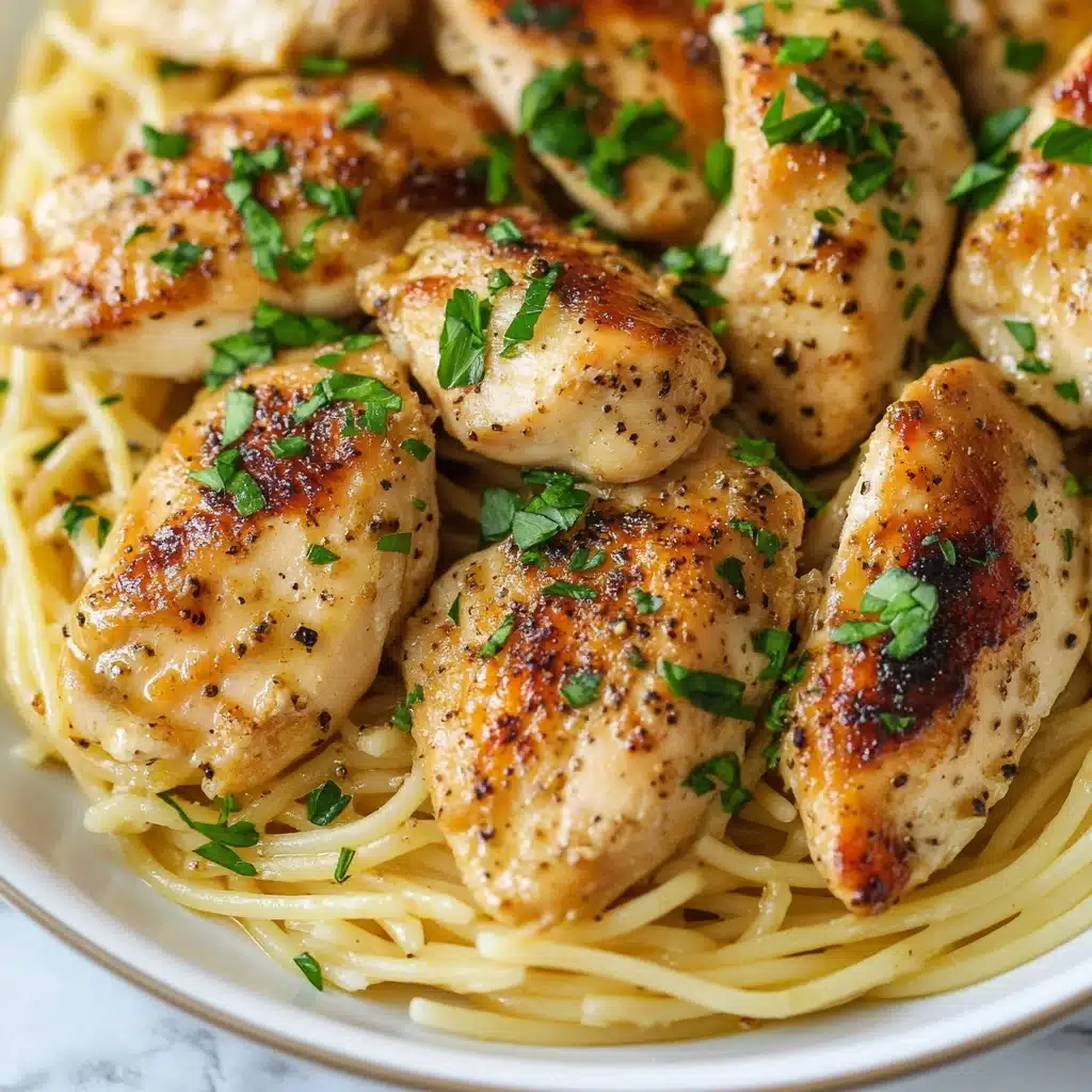 Chicken Scampi Pasta, easy chicken pasta recipes, lemon garlic chicken pasta, quick weeknight dinner, restaurant-style pasta The dish shows a white plate filled with a base layer of thin spaghetti noodles that are light yellow and smooth. On top, there are several pieces of cooked chicken with a golden-brown crust that looks juicy and slightly seasoned with black pepper. The chicken pieces are spread evenly over the noodles, and small green bits of fresh parsley and tiny pieces of chopped garlic are sprinkled over everything, adding color and texture. The white marbled surface under the plate is softly visible.
