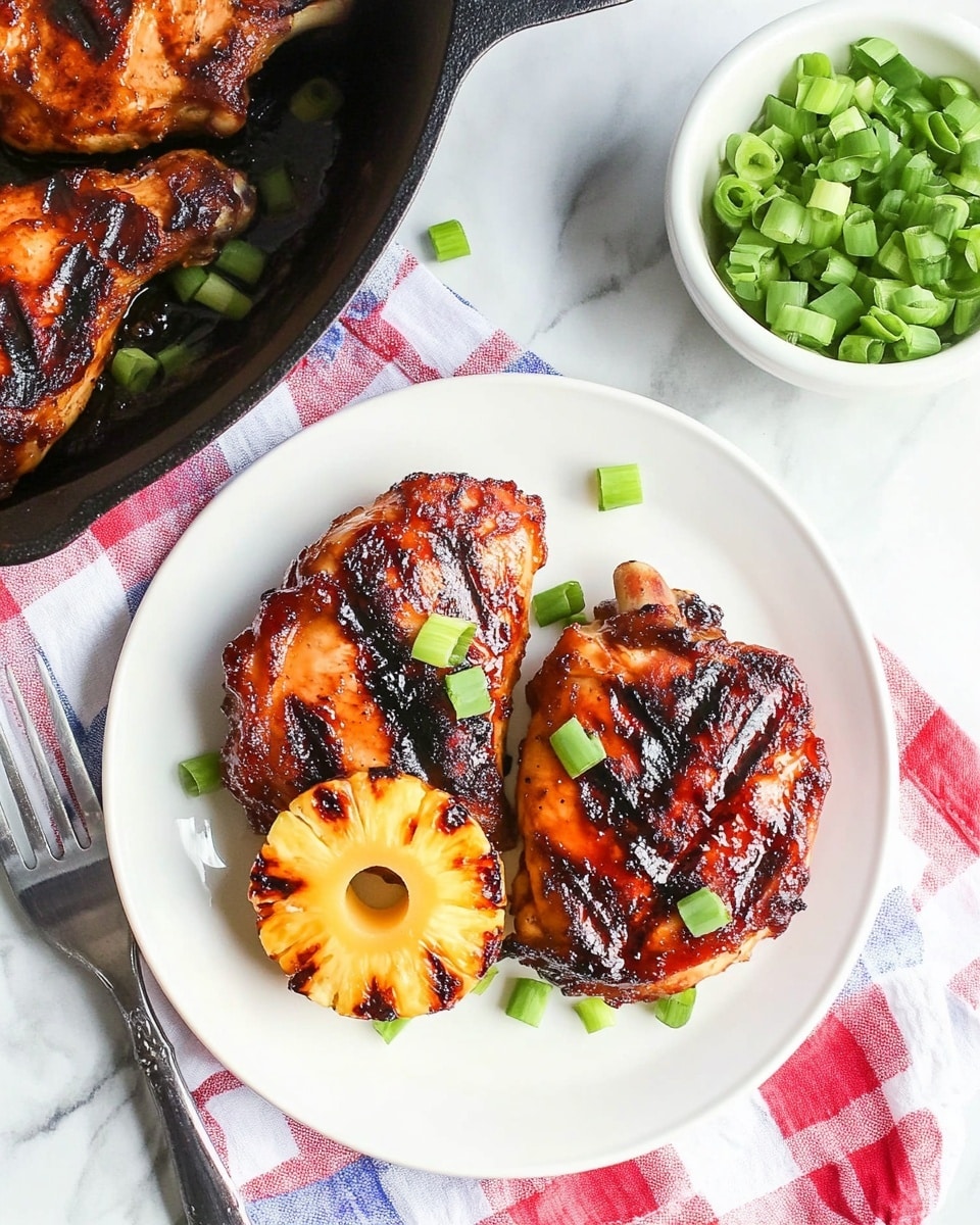 Sheet-Pan BBQ Pineapple Chicken, BBQ Pineapple Chicken, Pineapple Chicken with BBQ Sauce, Easy Sheet-Pan Chicken Dinner, Sweet Spicy Pineapple Chicken The image shows a white plate with two pieces of grilled chicken that have a charred, reddish-brown surface, topped with two bright yellow, juicy pineapple rings. Small green onion rings are scattered over the chicken and around the plate. Next to the plate, there is a white bowl filled with green onion rings, a silver fork resting on a red, white, and blue checkered cloth on a white marbled surface. In the top left corner, part of a black cast iron skillet is visible, containing more grilled chicken pieces and pineapple rings, also garnished with chopped green onions.