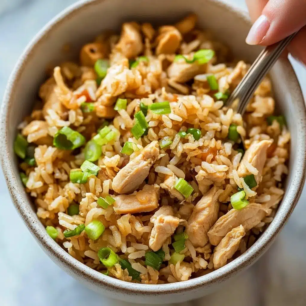 Chicken Fried Rice, quick fried rice recipe, easy weeknight dinner, flavorful fried rice, homemade fried rice A white bowl filled with cooked rice mixed with small pieces of chicken and chopped green onions. The rice is light brown, showing it is fried or cooked with sauce. On top are small slices of light green onions adding freshness. The chicken pieces are light tan, scattered evenly throughout the rice. A woman's hand holds a spoon inside the bowl, ready to scoop. The bowl sits on a white marbled surface.