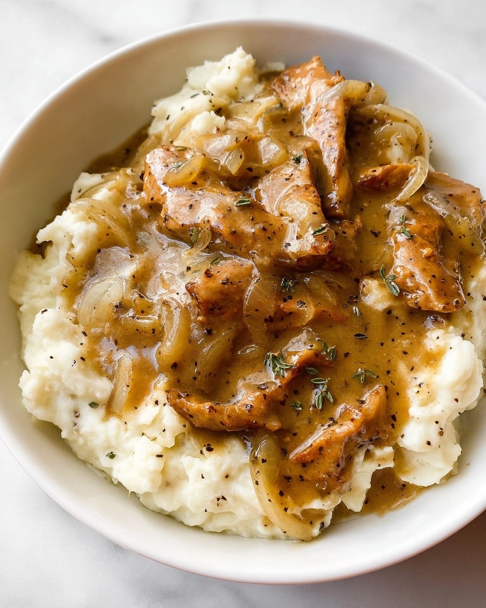 The dish shows two layers in a white bowl placed on a white marbled surface. The bottom layer is creamy mashed potatoes, white with a smooth and slightly lumpy texture. The top layer is covered with brown gravy that has a shiny, thick texture and visible black pepper specks. Inside the gravy are tender, thin slices of meat, light brown with some darker seared edges, and pieces of cooked onions that are translucent and light brown. The gravy is spread unevenly over the mashed potatoes, creating a cozy, homemade look. photo taken with an iphone --ar 4:5 --v 7