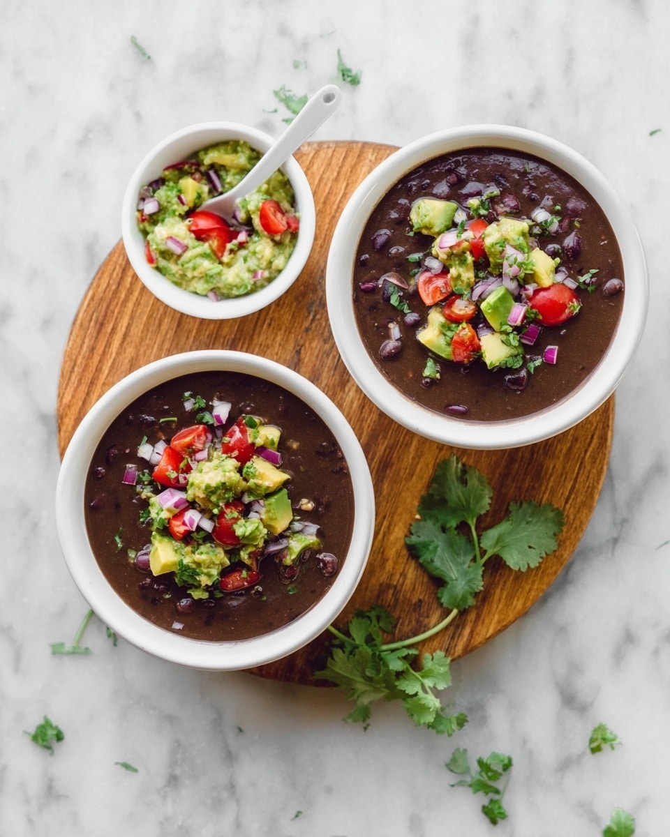 Two white bowls filled with thick, dark brown black bean soup sit on a round wooden board over a white marbled surface. Each bowl has a colorful topping of chunky guacamole made of bright green avocado pieces, red cherry tomato halves, and bits of purple onion scattered on top. Next to the bowls, a small white bowl with the same guacamole and a white spoon is placed. Fresh green cilantro sprigs are used as garnish around the wooden board. Photo taken with an iphone --ar 4:5 --v 7