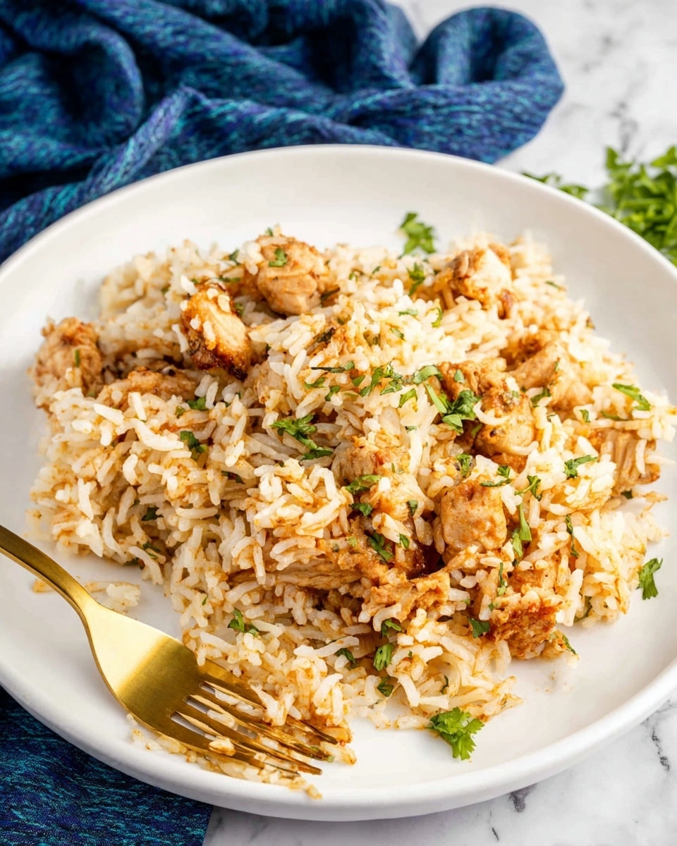A white plate holds a serving of cooked rice mixed with browned pieces of chicken, both coated lightly in a reddish-brown sauce. The rice grains are separate and fluffy, with small green herb bits sprinkled across the dish. A gold-colored fork rests on the plate, with some rice and chicken pieces on its tines. The plate sits on a white marbled surface, and a blue cloth is blurred in the background. photo taken with an iphone --ar 4:5 --v 7