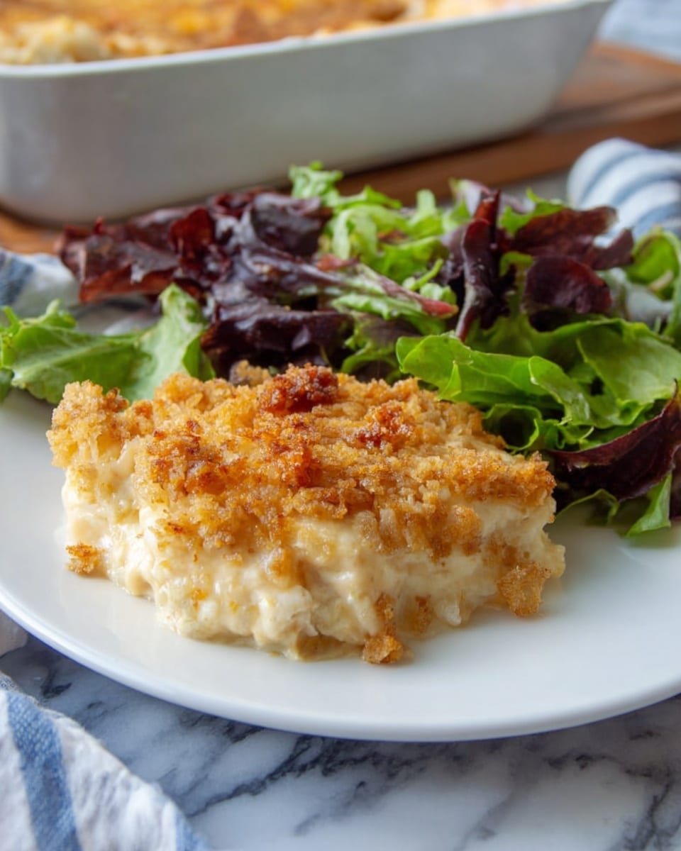 A white plate holds a serving of creamy casserole with a golden-brown crumb topping as the main layer, textured with small crispy bits. Behind it is a fresh side salad with mixed green and purple lettuce leaves, adding contrast with their vibrant colors. The background features a white marbled surface, and a casserole dish is partially visible at the top left. photo taken with an iphone --ar 4:5 --v 7