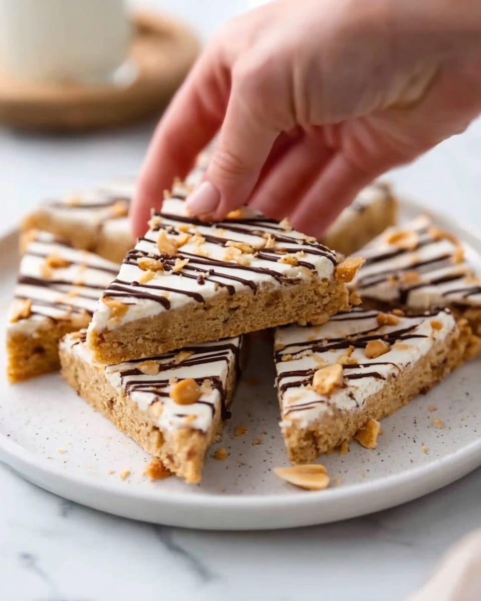 A white plate on a white marbled surface holds triangular cookie bars with a light brown base layer that looks soft and slightly crumbly, studded with small peanut chunks. The top layer is a smooth white frosting with thin, dark brown chocolate stripes drizzled across it in a zigzag pattern. A woman's hand is picking up one of the triangular pieces from the plate. Photo taken with an iphone --ar 4:5 --v 7
