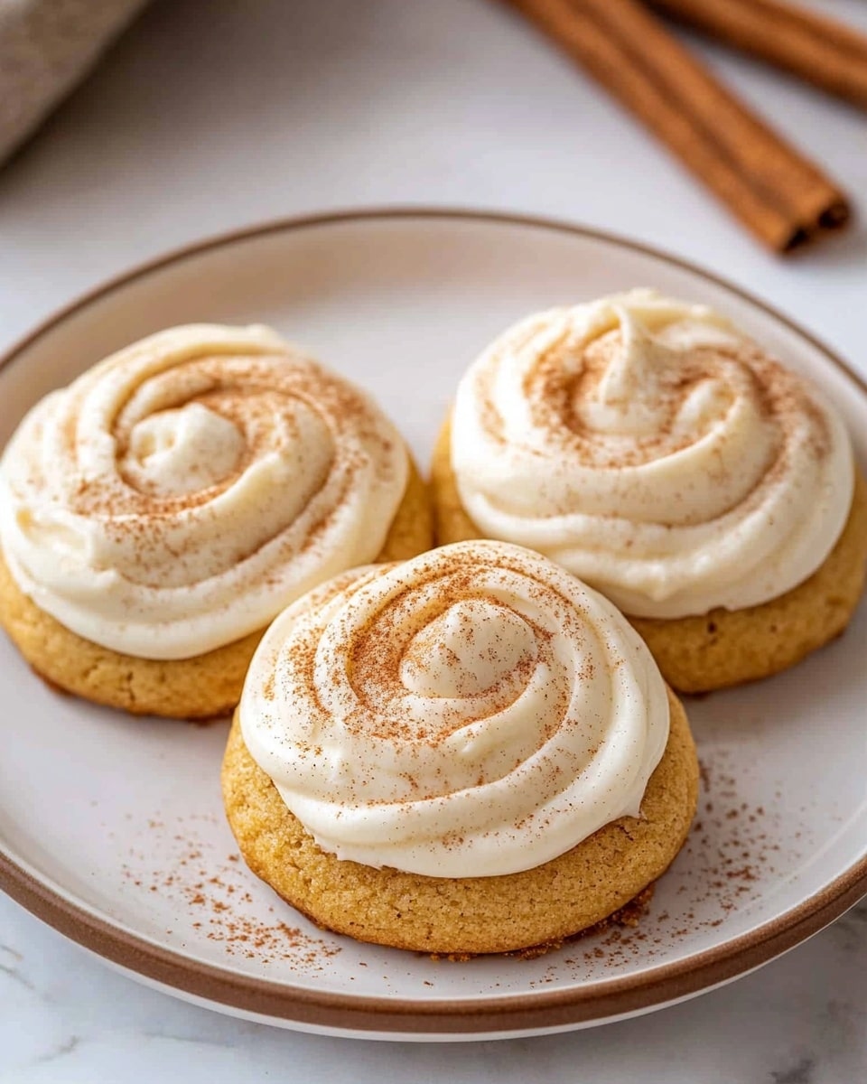 The image shows two stacked orange pumpkin cookies with a creamy white frosting layer on top and between them. The top cookie has a bite taken out, revealing a soft, textured inside. The frosting is thick and swirled with a light dusting of cinnamon powder on top. Next to the cookies, two cinnamon sticks rest on the white plate. The plate is set on a white marbled surface, creating a clean and cozy look. photo taken with an iphone --ar 4:5 --v 6.1