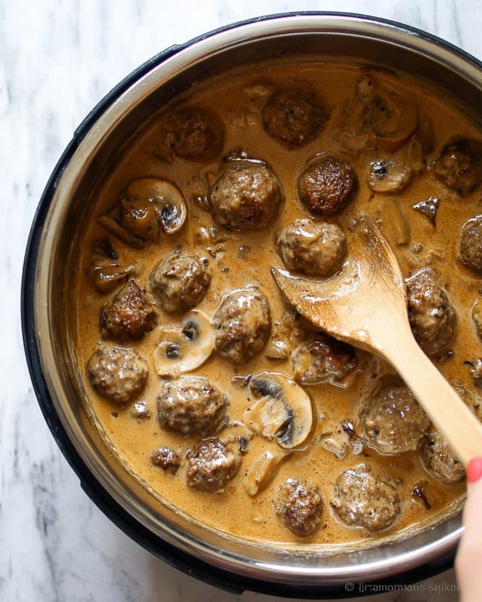 The image shows a pot filled with a thick, brown sauce with visible meatballs and sliced mushrooms floating in it. The sauce has a creamy texture with a slightly shiny surface. The meatballs are medium-sized, browned on the outside, and scattered throughout the sauce. Several light brown and white mushroom slices are mixed evenly into the dish. A wooden spoon is partially submerged, mixing the sauce and meatballs. The pot edge is silver and black, contrasting with the creamy sauce inside. The photo is taken with a woman's hand gently holding the spoon. The background is a white marbled texture photo taken with an iphone --ar 4:5 --v 7