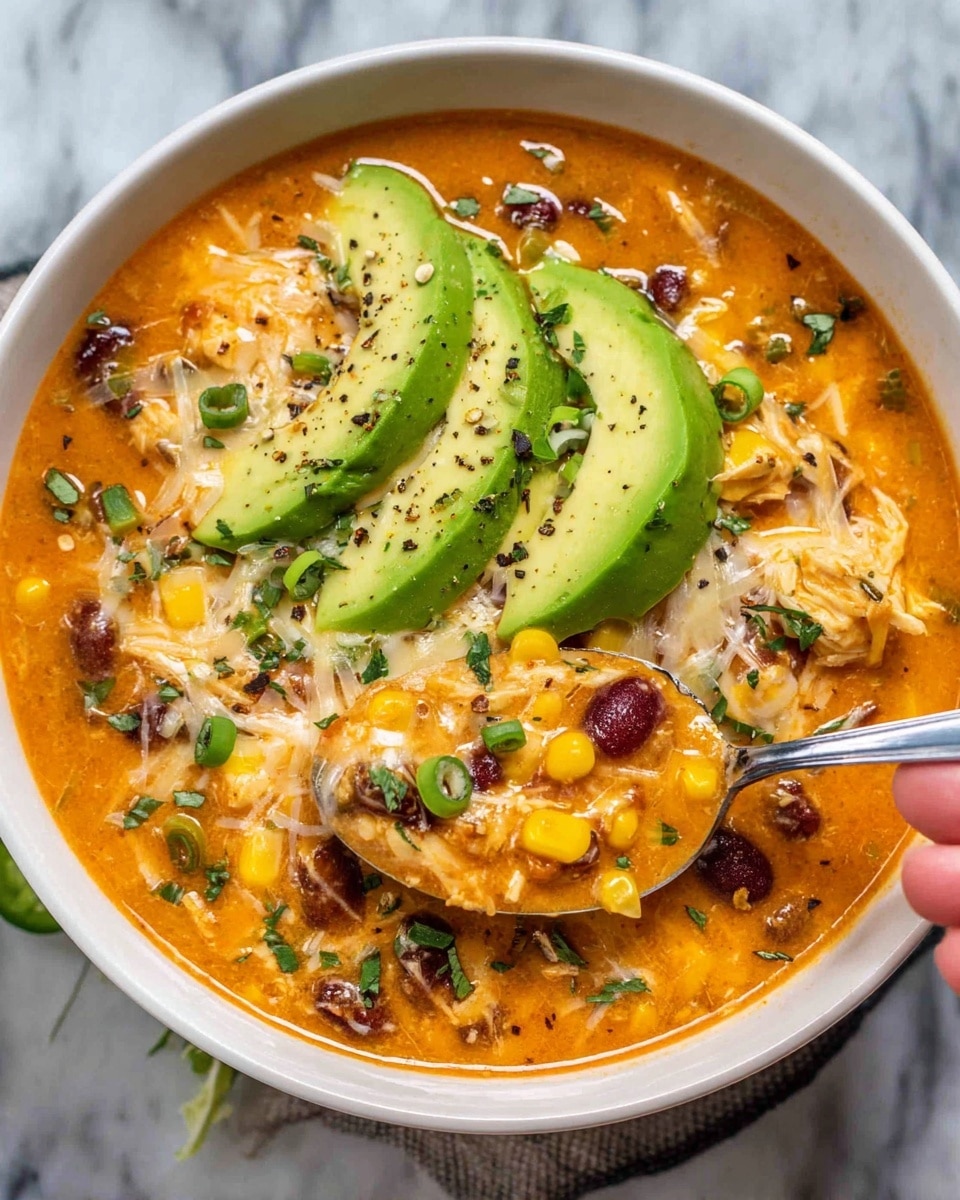 A white bowl filled with thick orange soup that has visible yellow corn kernels, dark red beans, and white shredded cheese melted on top. In the center, there are three slices of fresh green avocado sprinkled with black pepper and small green onion pieces. There are also slices of green jalapeño peppers and finely chopped herbs scattered on the surface. A spoon scoops some soup, showing a mix of corn, beans, chicken, and cheese, all covered in the orange broth, held by a woman's hand. The bowl is placed on a white marbled surface. photo taken with an iphone --ar 4:5 --v 7