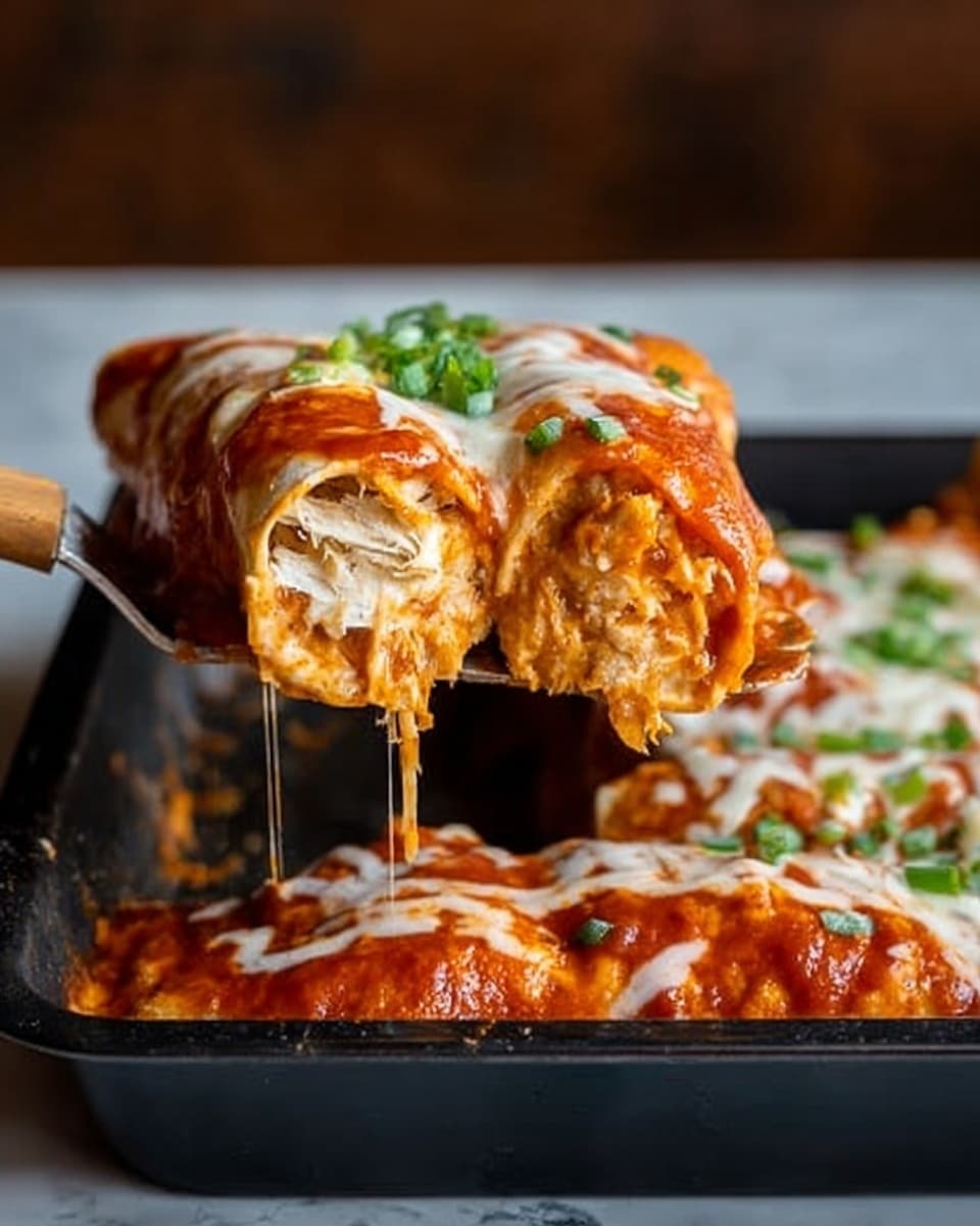 A close-up image of an enchilada being lifted from a black baking tray with a spatula. The enchilada has two visible layers: the inner layer is light beige with shredded filling, and it is wrapped in a soft tortilla. The outer layer is covered with a thick, rich red sauce and melted white cheese topped with small green onions. The baking tray has more enchiladas covered with the same sauce and toppings. The background is a white marbled surface with a blurred brown wall behind it. Photo taken with an iphone --ar 4:5 --v 7