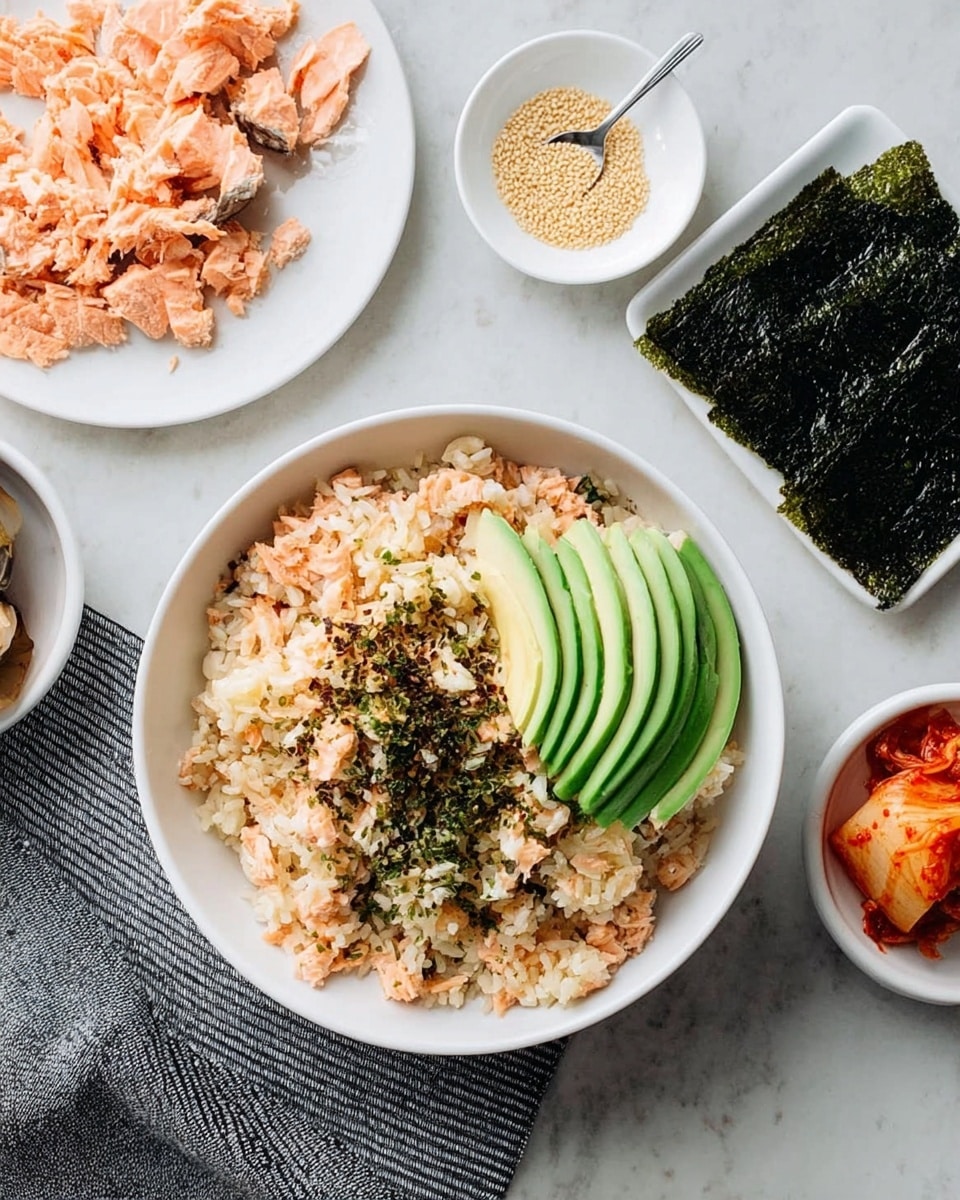 A woman's hand holds a small seaweed sheet layered with a base of cooked rice mixed with small pieces of light brown cooked fish, topped with a layer of bright green avocado and a small amount of reddish-orange kimchi with visible chili flakes. In the blurred background, there is a white bowl filled with more of the rice and fish mixture, garnished with several fanned slices of avocado on top. The whole scene is set on a white marbled surface with other bowls and ingredients softly visible around. Photo taken with an iphone --ar 4:5 --v 7