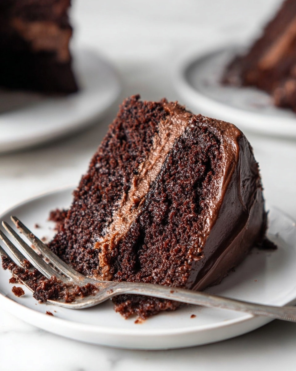 The image shows a close-up of a two-layer chocolate cake slice on a white plate, placed on a white marbled surface. The cake layers are dark brown with a moist, crumbly texture. Between the layers is a lighter brown chocolate filling that looks creamy and smooth. The outside of the slice is covered with a thick layer of the same dark chocolate frosting. A silver fork with some chocolate crumbs rests on the plate near the cake. In the background, there are blurred white plates each holding another piece of the cake. photo taken with an iphone --ar 4:5 --v 7
