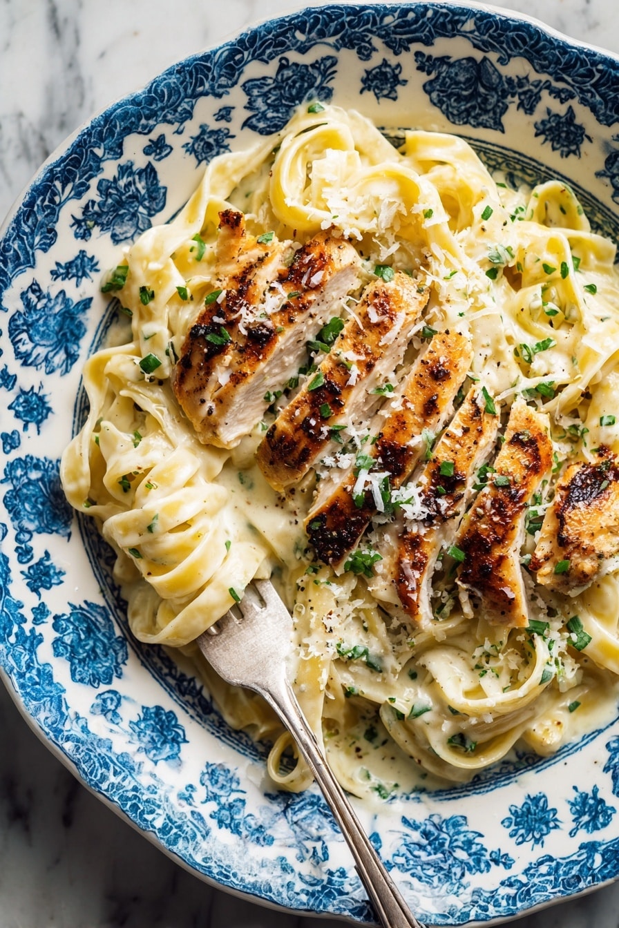 A close-up top view of a white plate with blue patterns filled with three main layers: the bottom layer is creamy, light yellow fettuccine pasta covered in a sauce with a smooth texture; on top of the pasta is a layer of thinly sliced grilled chicken with a golden brown, slightly crisp surface showing grill marks; sprinkled over both pasta and chicken are small pieces of chopped green herbs and finely grated white cheese. A silver fork is stuck into the pasta on the left side of the plate, some pasta twirled around its prongs. The plate sits on a white marbled textured surface. Photo taken with an iphone --ar 2:3 --v 7 - Healthy Chicken Alfredo, healthy creamy chicken pasta, easy chicken Alfredo, light chicken Alfredo dinner, quick healthy chicken recipe