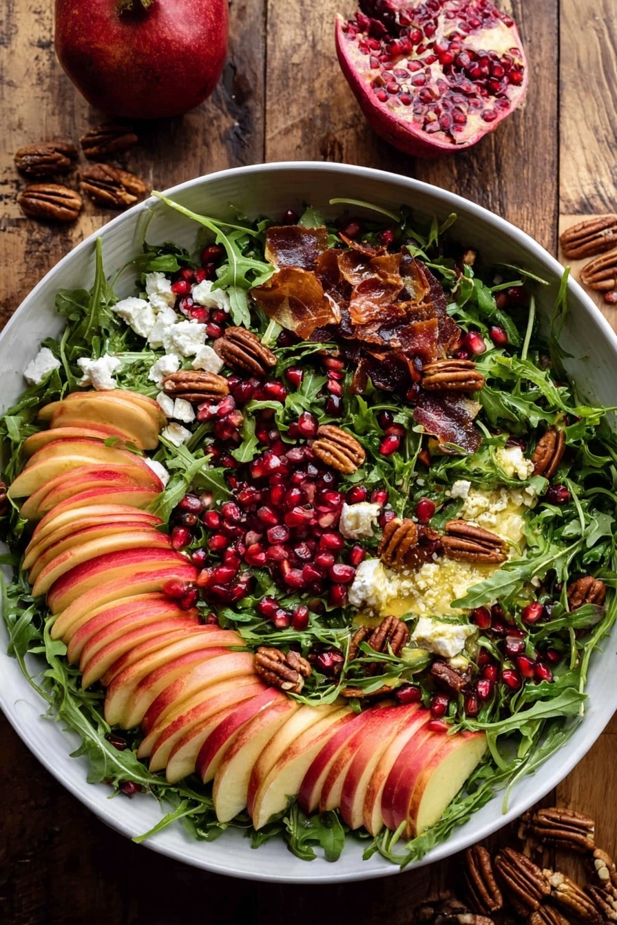A large white bowl filled with a colorful salad resting on a wooden surface. The base layer is fresh green arugula leaves spread evenly, topped with neatly sliced red and light yellow apples arranged in fanned clusters scattered throughout. Small bits of white cheese are sprinkled over the salad, adding contrast. There are dark red pomegranate seeds dotted across the salad, mixed with toasted nuts that add a crunchy texture and deep brown color. Pieces of crispy, thin slices of brown bacon or prosciutto are interspersed, giving extra warmth to the colors. Two wooden salad spoons with smooth handles rest inside the bowl on opposite sides. In the background, half a pomegranate with bright red seeds is on a white plate, along with small bunches of fresh green herbs and a few stray nuts. The whole scene is against a white marbled texture. photo taken with an iphone --ar 2:3 --v 7 - Autumn Harvest Honeycrisp Apple and Feta Salad, honeycrisp apple salad, fall apple salad recipes, seasonal apple feta salad, healthy autumn salads