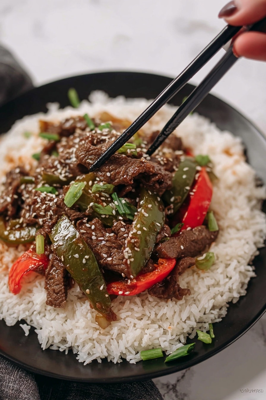 A white plate holds a large base layer of fluffy, long-grain white rice, spread evenly across the plate. On top of the rice sits a colorful stir-fry with three distinct elements: dark brown thin strips of cooked beef, glossy green bell pepper slices, and bright red bell pepper slices. The stir-fry is sprinkled with small white sesame seeds and chopped green onion pieces for freshness. Two black chopsticks rest across the top edge of the plate. The background shows a red bell pepper and green leafy herbs on a white marbled surface. Photo taken with an iphone --ar 2:3 --v 7 - Crockpot Pepper Steak, Slow Cooker Beef and Bell Pepper, Easy Crockpot Beef Stir Fry, Savory Pepper Steak Recipe, Tender Beef Crockpot Dinner