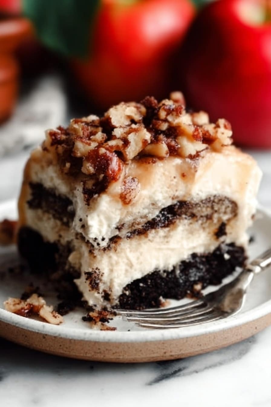 The image shows a close-up of a thick slice of layered dessert on a white plate. The bottom layer is dark and crumbly, looking like crushed chocolate cookies. Above that, there is a creamy, light beige layer that looks soft and smooth. On top, there is a sprinkle of chopped nuts mixed with small crumb pieces, giving a crunchy texture. A metal fork rests on the plate near the dessert. The background has a white marbled surface, and there are whole red apples blurred in the background. Photo taken with an iphone --ar 2:3 --v 7 - Apple Pie Cinnamon Rolls with Apple Cider Caramel Sauce and Cream Cheese Frosting, apple cinnamon roll recipe, fall dessert ideas, apple pie cinnamon rolls, caramel and cream cheese frosting