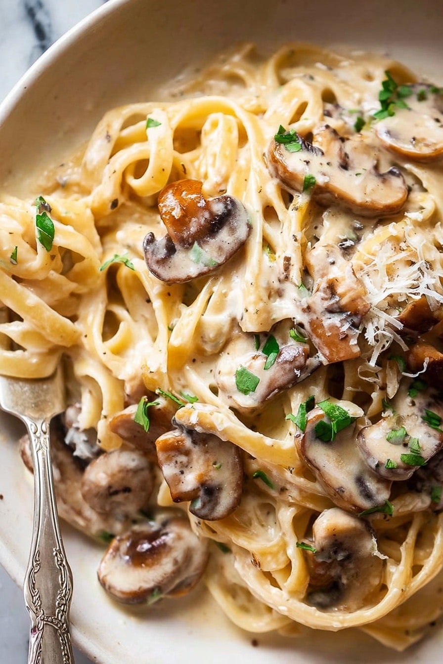 A close-up of creamy pasta with several long, flat noodles twisted and layered, covered in a smooth, off-white sauce. On top and mixed into the pasta are many thin slices of cooked mushrooms with a light brown color and soft texture. Small pieces of fresh green herbs are scattered over the whole dish, adding a splash of color. The dish is on a white plate with a fork partially wrapped in the pasta at the bottom left corner. The background is a white marbled texture. Photo taken with an iphone --ar 2:3 --v 7 - Creamy Mushroom Pasta, mushroom pasta recipe, easy mushroom pasta, quick creamy pasta, vegetarian mushroom pasta