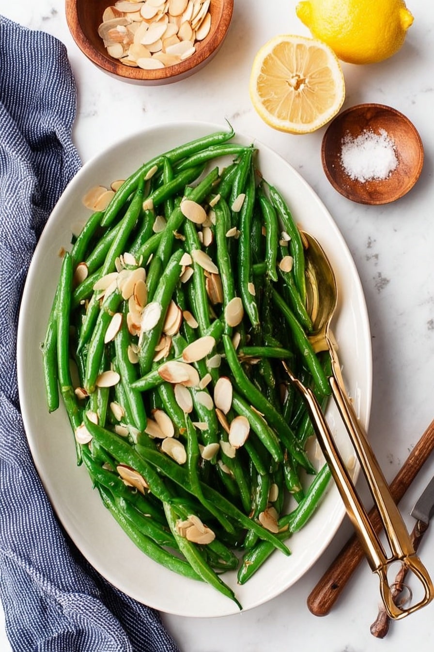 A close-up view of a black cast iron skillet filled with bright green cooked green beans mixed with thin slices of cooked white onions. A light-colored wooden spatula with visible grain rests on top of the green beans, placed in the center of the skillet. The skillet sits on a white marbled surface with a light gray cloth partially visible behind it. To the upper right, there is a wooden spoon holding two halves of a yellow lemon. At the bottom of the image, two small wooden objects are slightly visible. The whole scene has soft, natural light highlighting the fresh textures. photo taken with an iphone --ar 2:3 --v 7 - Green Beans Almondine with Toasted Almonds, green beans almondine, lemon green bean side dish, almond-sautéed green beans, elegant vegetable side dish