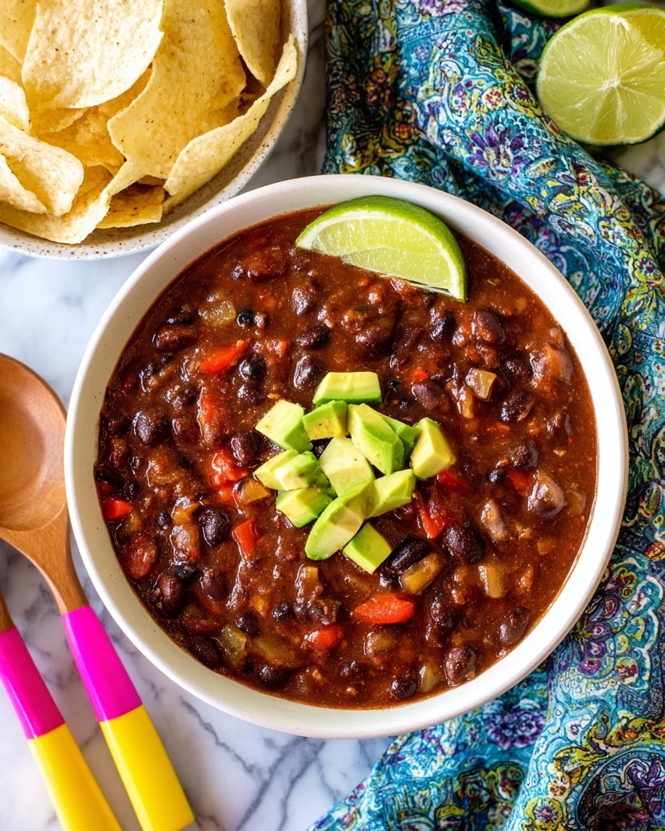 A white bowl filled with three layers: the bottom layer is thick chili with dark brown beans and red pieces in a rich tomato sauce, the middle layer is a topping of bright green avocado chunks in the center, and the top layer is a lemon wedge resting on the rim of the bowl. Another identical bowl is blurred in the background, both placed on a white marbled surface with colorful cloths around. Photo taken with an iphone --ar 4:5 --v 7
