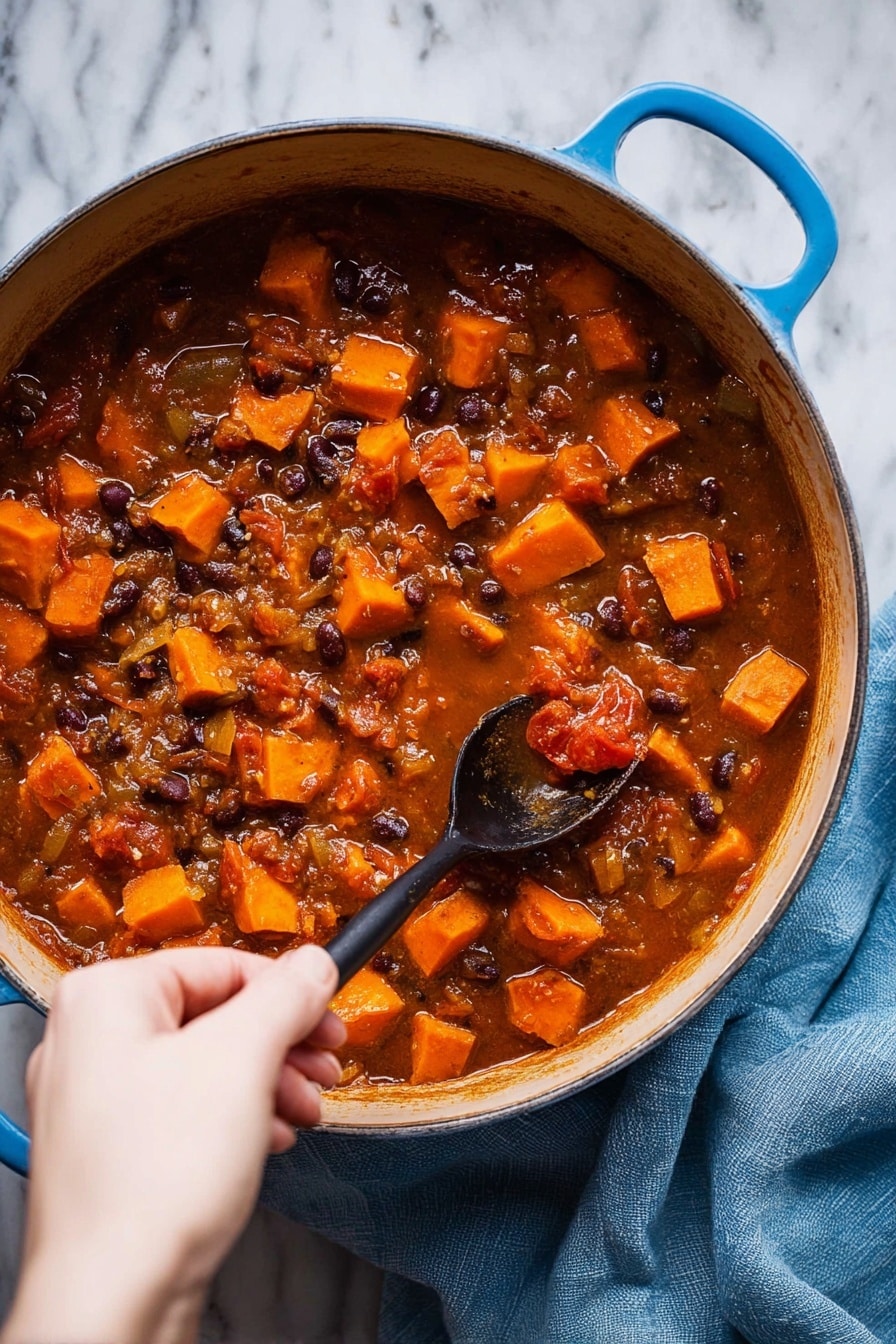 A large blue pot filled with a thick rich stew that has many small orange cubes of sweet potato, dark beans, and pieces of tomato in a brownish-red liquid. The stew has visible chunks of onion and a textured look from the cooked ingredients. A woman's hand is holding a black spoon, stirring the stew gently. The pot is placed on a white marbled surface, with a soft blue cloth nearby. Photo taken with an iphone --ar 2:3 --v 7 - Sweet Potato Black Bean Soup, Healthy vegan soup recipe, Easy vegetarian soup, Nutritious black bean soup, Comforting plant-based dinner