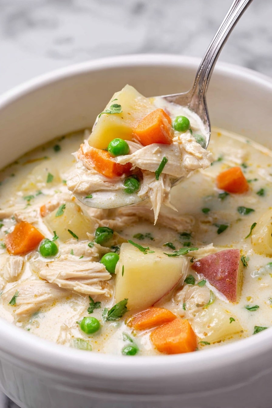 A white bowl filled with thick creamy chicken soup shows several layers: the base is a light cream broth, with chunks of light beige shredded chicken, bright orange carrot slices, small green peas, and white potato pieces with reddish skin. A silver spoon lifts a scoop of the soup, filled with all these colorful ingredients, positioned slightly above the bowl. The background is a white marbled texture, giving a clean and fresh look to the image. Photo taken with an iphone --ar 2:3 --v 7 - Slow Cooker Garlic Parmesan Chicken Stew, Creamy Chicken Stew with Parmesan, Easy Slow Cooker Chicken Recipes, Comfort Food Chicken Stew, Garlic Parmesan Chicken Dinner