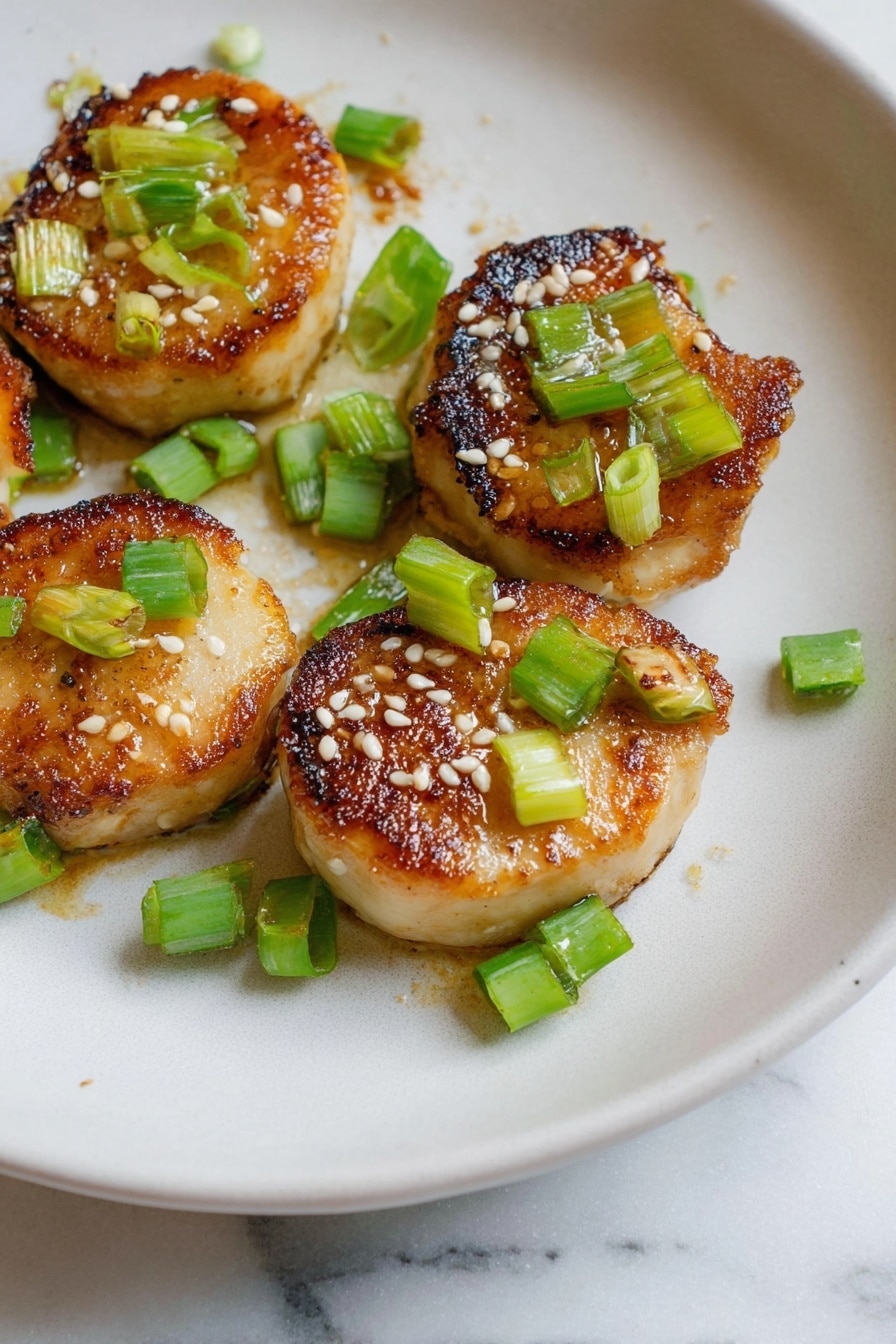 The image shows five small round pieces of golden-brown cooked food with a slightly crispy and caramelized texture on top. Each piece is garnished with small green chopped scallions and sprinkled with white sesame seeds. They are arranged on a white plate with a smooth, slightly matte surface, placed on a white marbled textured background. The food looks warm and freshly cooked, with the colors of golden brown, light green, and white creating a fresh and appetizing look. photo taken with an iphone --ar 2:3 --v 7 - Miso Soy King Oyster Mushroom, vegan scallops, plant-based seafood, mushroom scallops recipe, umami mushroom dish