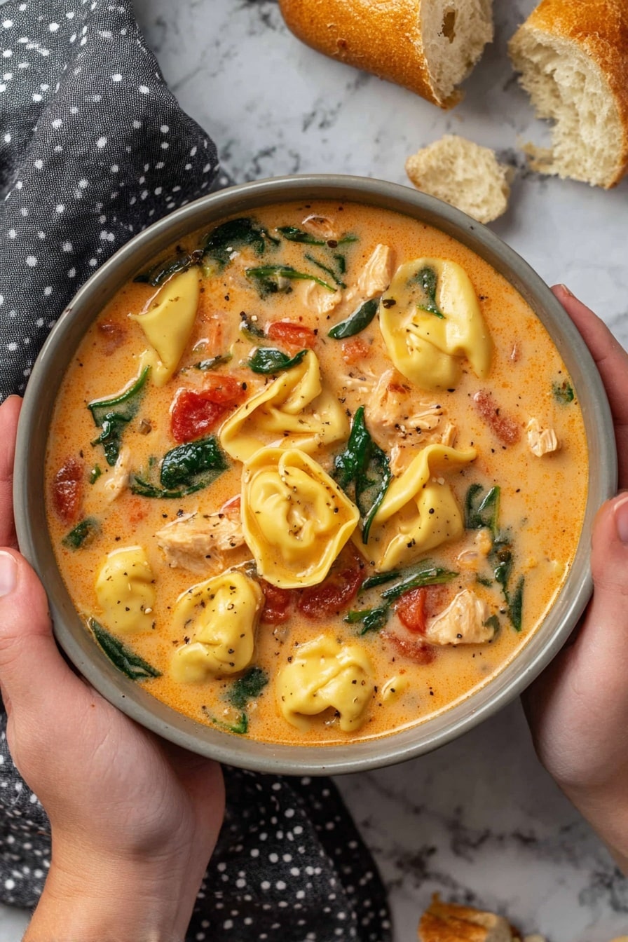 A black slow cooker filled with creamy orange soup containing plump yellow tortellini pasta, scattered fresh dark green spinach leaves, and small red tomato pieces mixed in a smooth sauce with visible bits of white shredded chicken, a curved wooden spoon resting inside the cooker, placed on a white marbled surface with pieces of toasted bread on a gray cloth nearby photo taken with an iphone --ar 2:3 --v 7 - Creamy Chicken Tortellini Soup, slow cooker tortellini soup, hearty chicken tortellini soup, easy crock pot tortellini, comforting chicken soup recipe