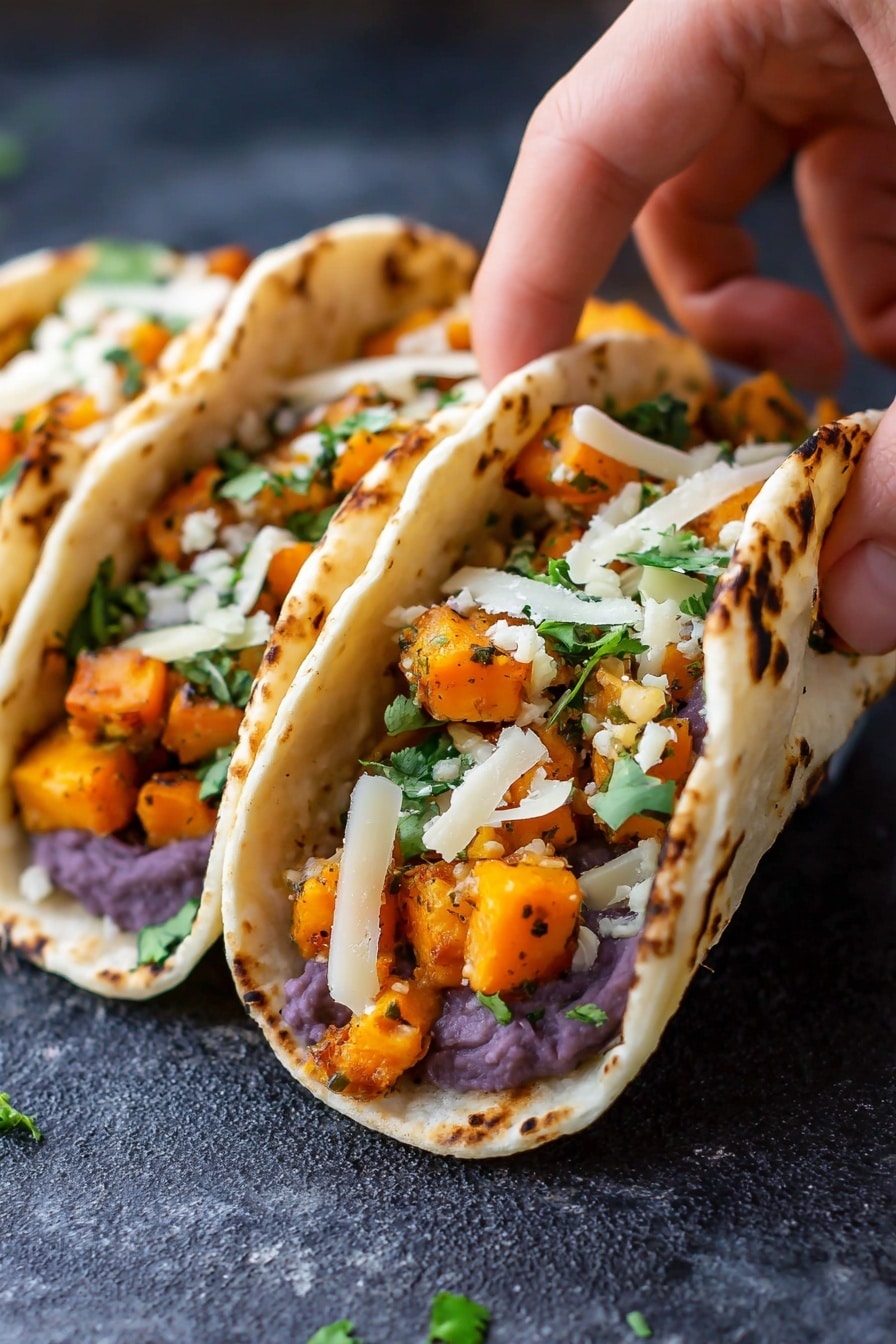 The image shows three small tacos placed closely side by side on a dark textured surface. Each taco has three layers: the bottom layer is a white corn tortilla with light brown spots from cooking, the middle layer is mashed purple beans spread evenly, the top layer consists of bright orange cubes of cooked squash mixed with small green cilantro leaves, and thin pale white strips of cheese scattered on top. A woman's hand is gently holding the front taco, lifting the tortilla slightly to reveal the filling inside. Photo taken with an iphone --ar 2:3 --v 7 - Black Bean Sweet Potato Tacos, vegetarian taco recipes, healthy taco ideas, quick dinner recipes, plant-based tacos