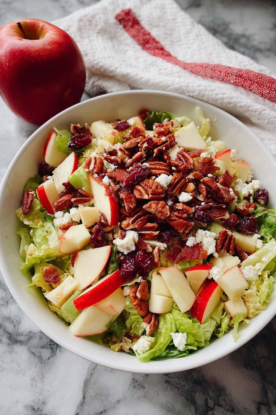 A white bowl holds a fresh salad with three main layers. The bottom layer is a mix of green lettuce leaves, light and crispy in texture. On top of the lettuce, there are chopped red and green apple pieces with smooth skin and crunchy texture. Scattered all over the apples and lettuce are small white crumbles of cheese and reddish dried cranberries. The top layer is made up of pecan nuts, brown and slightly rough, spread evenly across the surface. The bowl sits on a white marbled surface, next to a red apple and a white cloth with red stripes. Photo taken with an iphone --ar 2:3 --v 7 - Honeycrisp Harvest Salad, fall salad with apples, apple and bacon salad, Autumn fruit salad, easy apple salad recipe