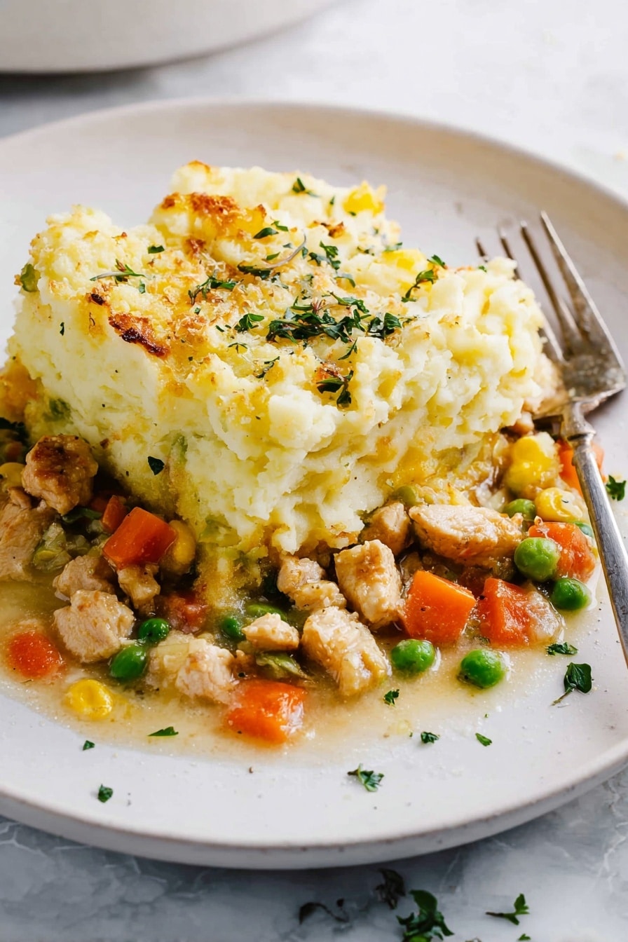 The dish shows two layers on a white plate with a white marbled surface below. The bottom layer is a mix of small pieces of light brown cooked chicken, bright orange carrot cubes, green peas, and some yellow bits, all in a light sauce. The top layer is a thick, fluffy heap of mashed potatoes with a pale yellow color and a slightly browned, baked texture on the edges. Small green herb pieces are sprinkled over the top and around the plate. A metal fork rests on the right side of the plate. photo taken with an iphone --ar 2:3 --v 7 - Healthy Turkey Shepherd's Pie, healthy shepherd's pie recipe, turkey comfort food, nutritious comfort dinner, light shepherd's pie