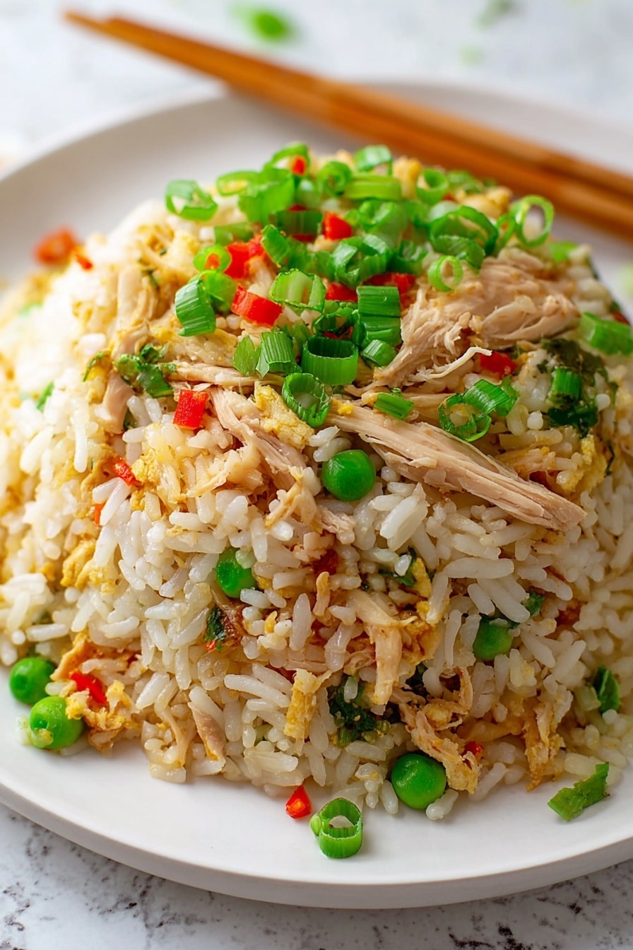 A close-up view of a mound of fried rice on a white plate, placed on a white marbled surface. The dish has three main layers: the bottom layer is white and slightly golden rice grains, the middle layer contains shredded light brown chicken pieces mixed with small green peas, and the top layer is scattered with bright green chopped spring onions and tiny red bell pepper bits. Wooden chopsticks rest diagonally at the back of the plate. Photo taken with an iphone --ar 2:3 --v 7 - Quick Chicken Fried Rice, easy chicken fried rice, fast fried rice recipe, beginner-friendly fried rice, leftover chicken dinner