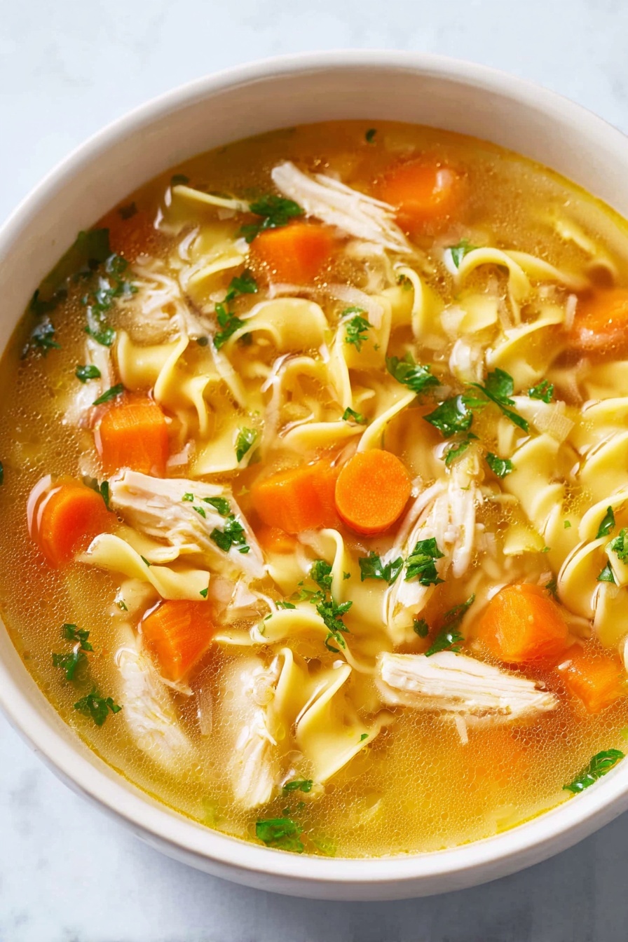 A white bowl filled with clear golden broth containing curly yellow noodles, bright orange carrot cubes, soft white onion pieces, light beige shredded chicken, and small green parsley leaves scattered on top, all resting on a white marbled surface photo taken with an iphone --ar 2:3 --v 7 - Homemade Chicken Noodle Soup, easy chicken noodle soup, comforting chicken noodle soup, homemade chicken broth, best chicken noodle soup