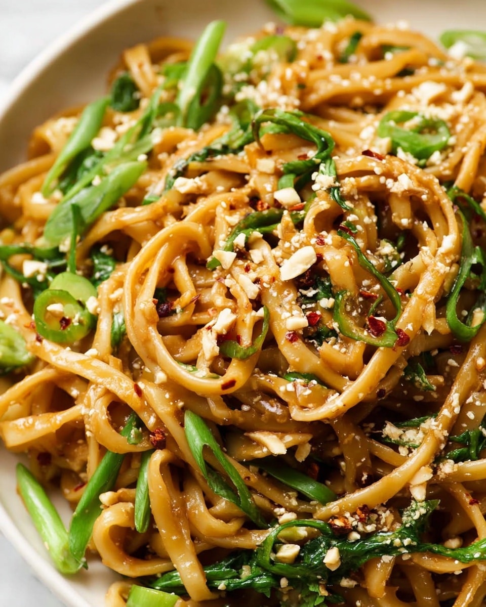 A bowl filled with golden brown noodles mixed with green peas and small herb leaves, topped with finely grated cheese that adds a light white dusting over the top. The noodles look slightly glossy and soft, sitting inside a white bowl on a white marbled surface. The photo was taken with an iphone --ar 4:5 --v 7