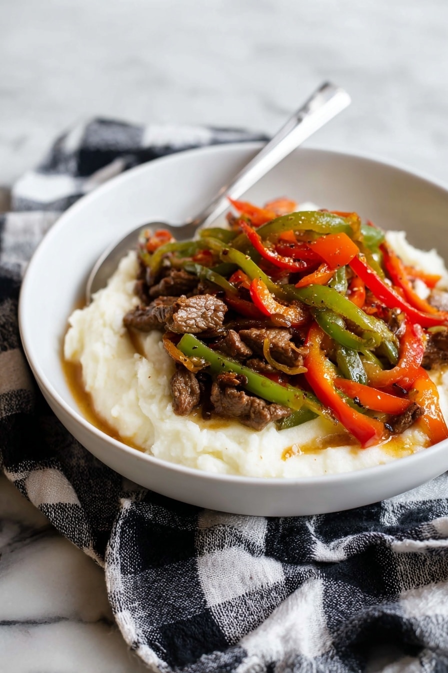 A white bowl holds a dish with two main layers: the bottom layer is a smooth, creamy white mashed texture, slightly spread around the edges. On top, there is a colorful mix of thin strips of cooked green, red, and orange bell peppers, mixed with small pieces of brown cooked meat, all glistening with a light sauce. A silver spoon rests inside the bowl, angled towards the back. The bowl sits on a black and white checkered cloth, placed on a white marbled surface. photo taken with an iphone --ar 2:3 --v 7 - Pepper Steak with Onion, pepper steak recipe, easy beef stir-fry, flavorful steak dinner, quick weeknight steak
