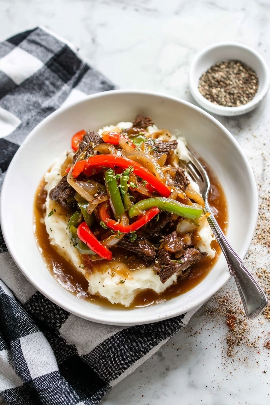 A white shallow bowl holds a layered dish with mashed potatoes at the bottom, creamy white and soft in texture. On top, there are strips of beef cooked dark brown, mixed with sautéed red and green bell pepper slices, and translucent cooked onions. The layers are covered with a glossy brown gravy that pools slightly at the base. A silver fork rests on the edge of the bowl. The bowl sits on a black and white checkered cloth, placed on a white marbled surface. To the top right, there is a small white dish with cracked black pepper scattered around it. photo taken with an iphone --ar 2:3 --v 7 - Pepper Steak with Onion, pepper steak recipe, easy beef stir-fry, flavorful steak dinner, quick weeknight steak