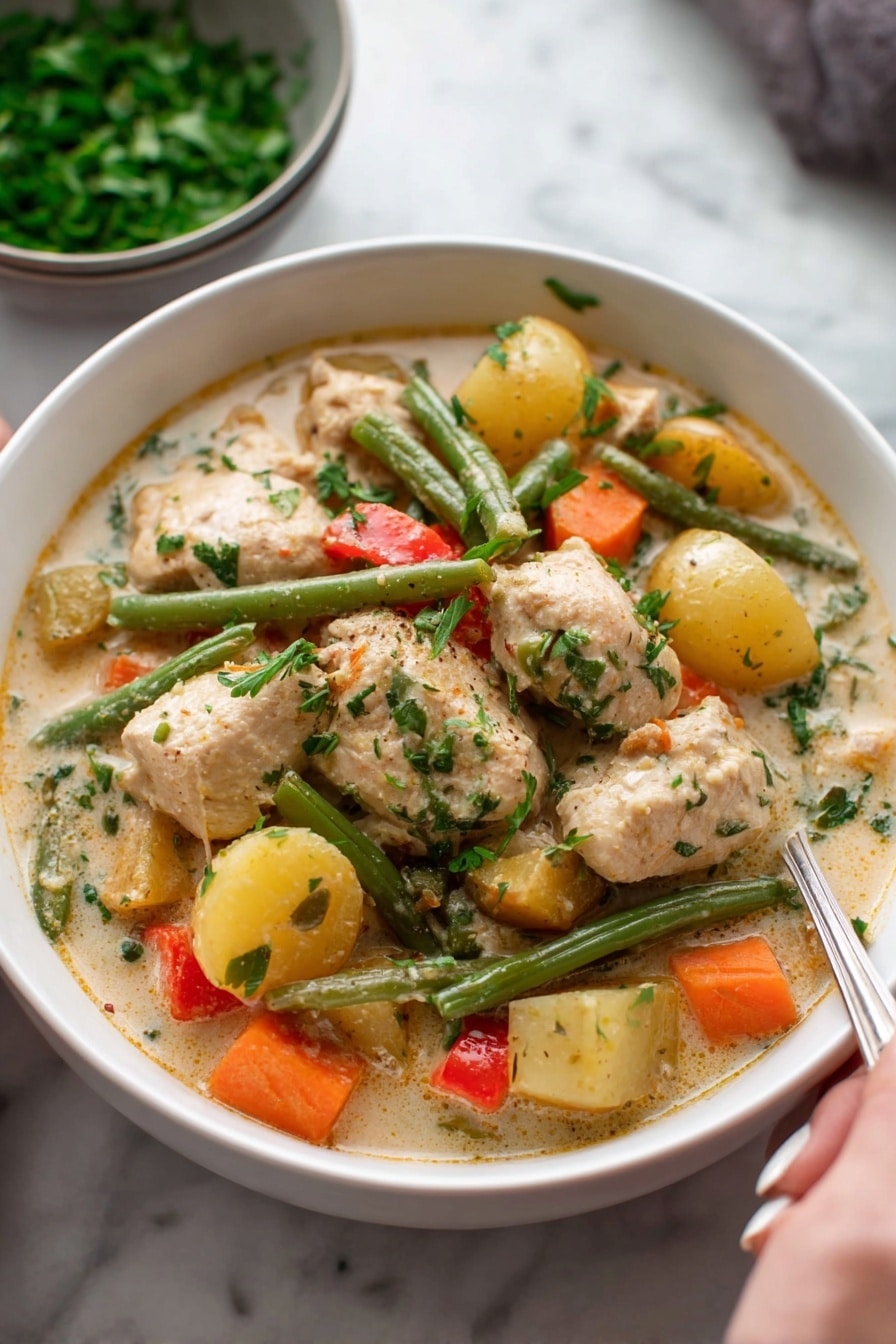 A white bowl filled with creamy chicken stew, showing large pieces of light brown chicken and chunky vegetables including orange carrots, green beans, yellow potatoes, and small bits of red pepper, all mixed in a thick, pale sauce with visible herbs on top; in the background, a bowl of chopped green herbs rests on a white marbled surface, and a woman's hand holding a spoon is partly visible at the bottom right. photo taken with an iphone --ar 2:3 --v 7 - Hearty Chicken and Vegetable Stew, Comforting chicken vegetable stew, Easy chicken stew recipe, Hearty winter stews, Healthy chicken vegetable dinner