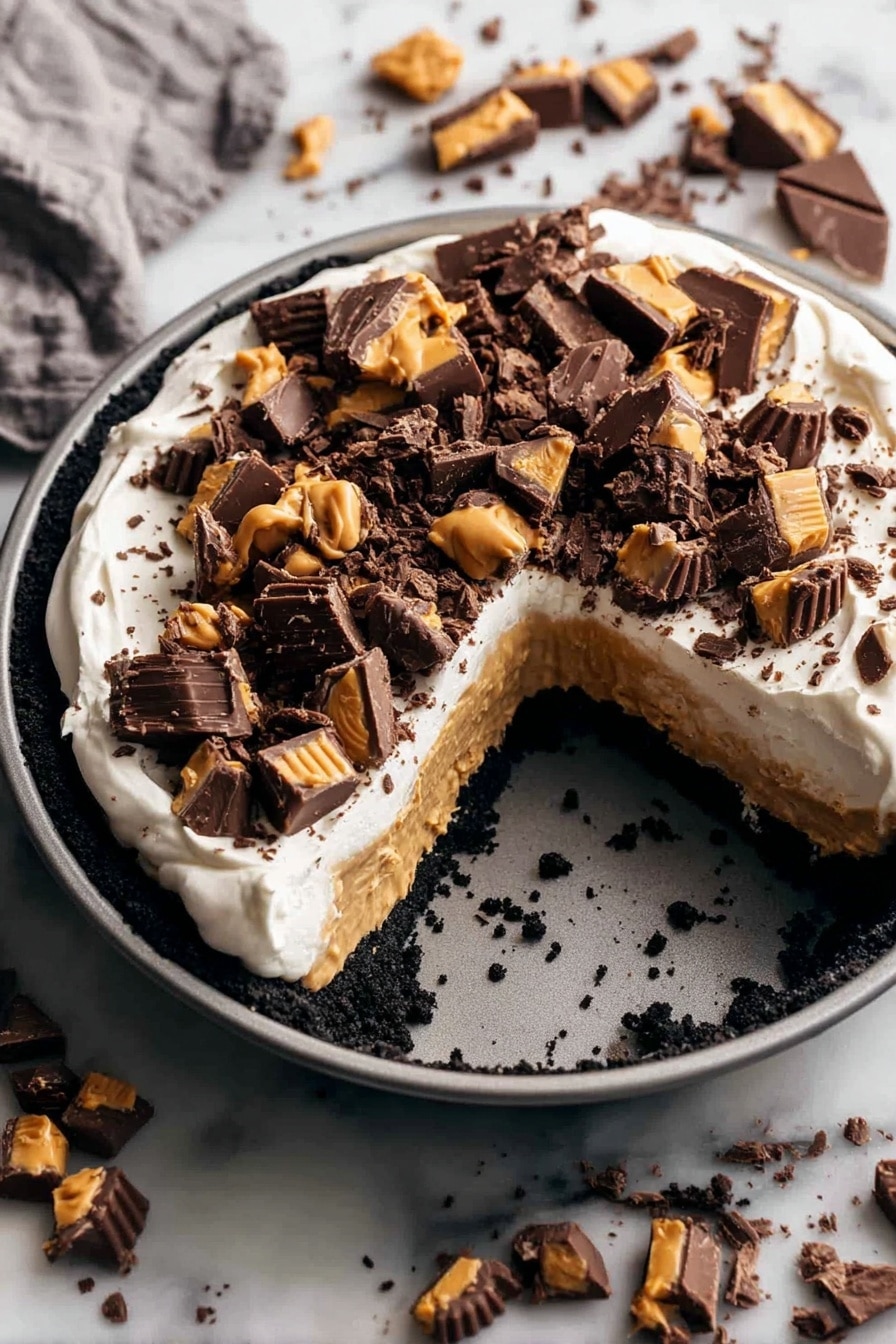 A round dessert in a gray pan has three layers: a dark crumbled base, a thick light brown peanut butter layer, and a smooth white cream layer on top. The cream is covered with many pieces of dark chocolate and peanut butter candy scattered unevenly. The pan is placed on a white marbled surface with more pieces of the same chocolate candy spread around it. A large wedge is missing from the dessert, showing the three colorful layers clearly. photo taken with an iphone --ar 2:3 --v 7 - Chocolate Peanut Butter Pie, chocolate peanut butter pie dessert, easy peanut butter chocolate pie, no-bake chocolate peanut butter pie, quick chocolate peanut butter pie