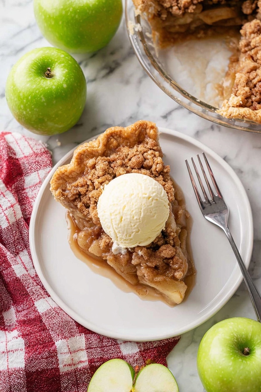 A white plate holds a single slice of apple crumble pie showing three visible layers: a golden brown crinkled crust on the outside edge, a thick middle layer of soft apple pieces coated in sticky brown sugar sauce, and a crumbly cinnamon topping in light and dark brown tones. On top of the pie slice sits a round scoop of creamy off-white vanilla ice cream that is starting to melt slightly. A silver fork lies diagonally on the plate pointing toward the bottom right corner. The plate rests on a white marbled surface surrounded by four whole shiny green apples and one apple cut in half showing pale yellow flesh inside. A red and white checkered cloth sits near the plate's bottom left corner. In the upper right corner, a glass pie dish contains the remaining apple crumble pie with a missing slice. Photo taken with an iphone --ar 2:3 --v 7 - Dutch Apple Pie, apple pie recipe, homemade apple pie, classic apple pie, easy apple pie dessert
