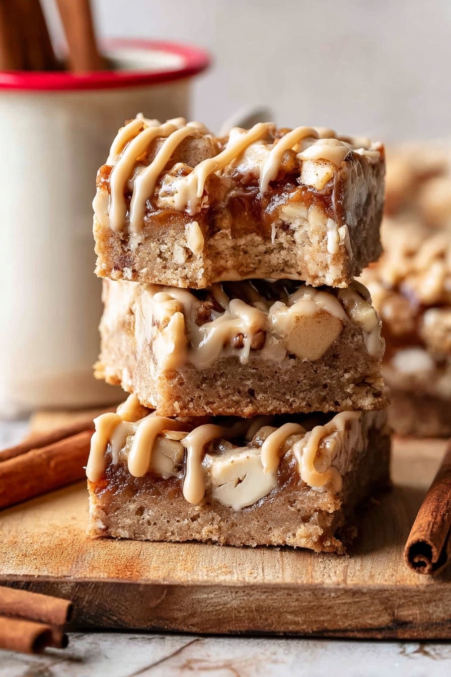 The image shows three square bars stacked vertically on a wooden surface with a single bite taken from the top bar. Each bar has a thick, crumbly base layer in light brown with small white nut pieces embedded inside. On top of the base, there is a layer of darker brown chunks with a soft texture, drizzled with thick, pale caramel-colored frosting in thin, uneven lines. A cinnamon stick is placed near the bottom left corner, and a white mug with a red rim and two cinnamon sticks inside is partially visible to the right. The background is a white marbled texture. Photo taken with an iphone --ar 2:3 --v 7 - Brown Butter Apple Blondies with Cinnamon Maple Glaze, fall dessert recipes, apple blondie recipes, cozy autumn desserts, easy apple blondies