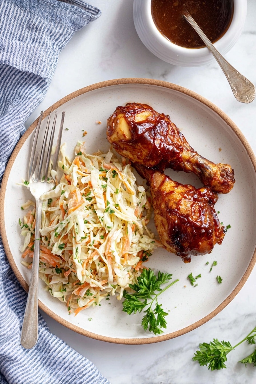 The image shows a white plate with two dark brown glazed chicken drumsticks placed on the right side. On the left side of the plate, there is a serving of creamy coleslaw made of shredded cabbage and carrots mixed with green herbs, creating a mix of white, orange, and green colors with a soft texture. A silver fork rests on the left edge of the plate, partly touching the coleslaw. A small sprig of fresh green parsley lies near the bottom right of the coleslaw. The plate is on a white marbled surface with a blue-striped cloth partially visible at the bottom left. To the top right, there is a white bowl filled with dark brown sauce with a spoon inside it. photo taken with an iphone --ar 2:3 --v 7 - Incredible Slow Cooker Drumsticks, easy slow cooker chicken recipes, 4-ingredient chicken dinner, juicy slow cooker drumsticks, simple slow cooker chicken legs