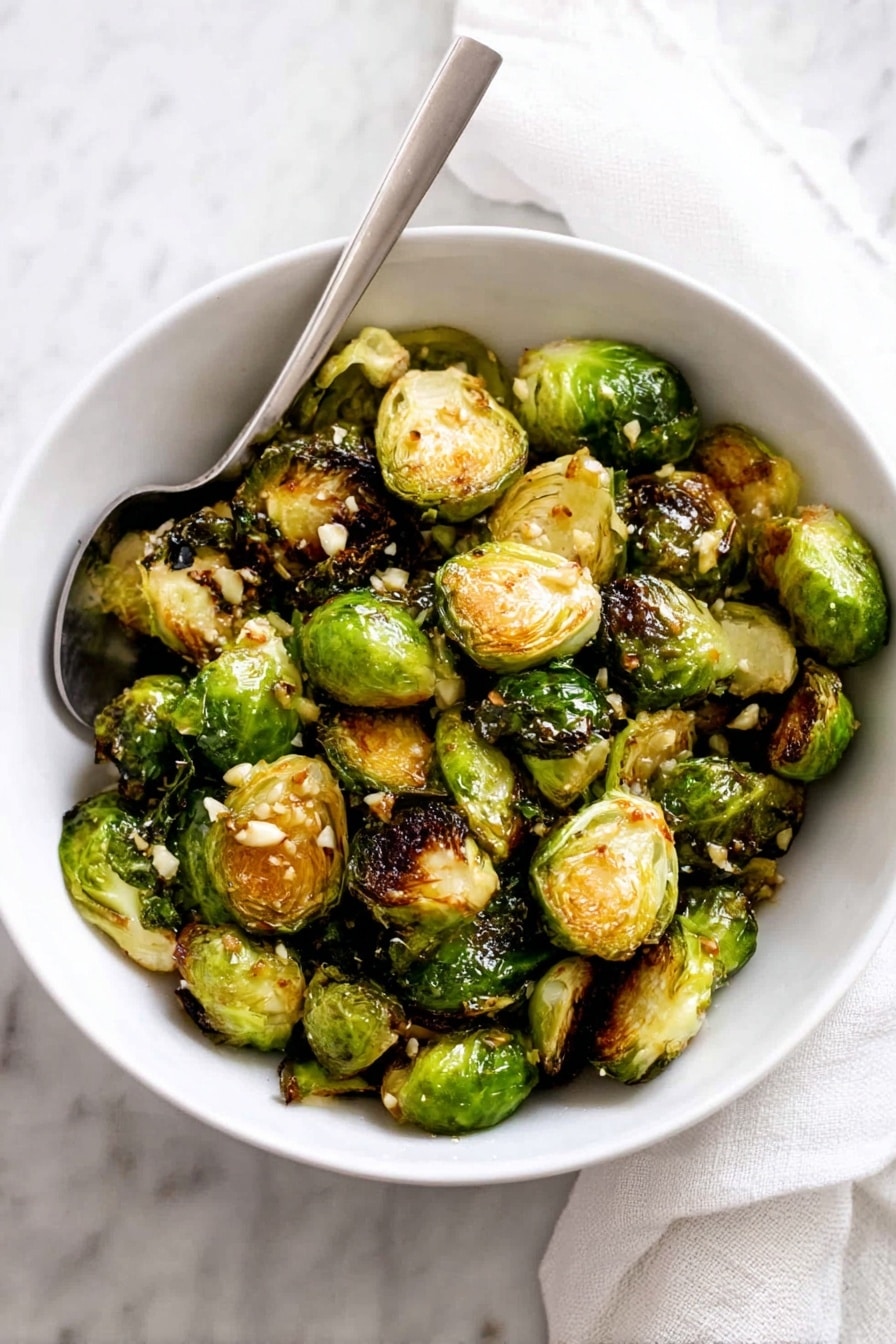 This close-up image shows several roasted Brussels sprouts resting on a white marbled surface. Each Brussels sprout is halved, revealing an inner layer of tightly packed leaves that are light green and yellow with caramelized, dark brown edges from roasting. Some outer layers are slightly charred and crispy, showing darker green and brown colors. Small bits of seasoning or salt are visible on the caramelized tops, adding texture and contrast. The moisture and oil around the sprouts create a slight shine, making the roasted texture stand out. photo taken with an iphone --ar 2:3 --v 7 - Garlic Honey Butter Roasted Brussels Sprouts, roasted Brussels sprouts, honey glazed Brussels sprouts, easy side dish recipes, flavorful vegetable side