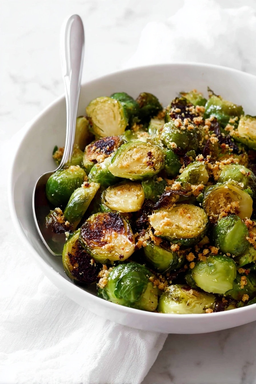 A white bowl filled with two layers of roasted Brussels sprouts, each piece halved to show a mix of light green interiors and crispy dark brown charred edges, giving a textured look; sprinkled with small bits of golden-brown garlic or breadcrumbs on top, a silver spoon placed inside the bowl rests against the side; the bowl is set on a white marbled surface with a white cloth nearby, creating a simple, clean setting. photo taken with an iphone --ar 2:3 --v 7 - Garlic Honey Butter Roasted Brussels Sprouts, roasted Brussels sprouts, honey glazed Brussels sprouts, easy side dish recipes, flavorful vegetable side