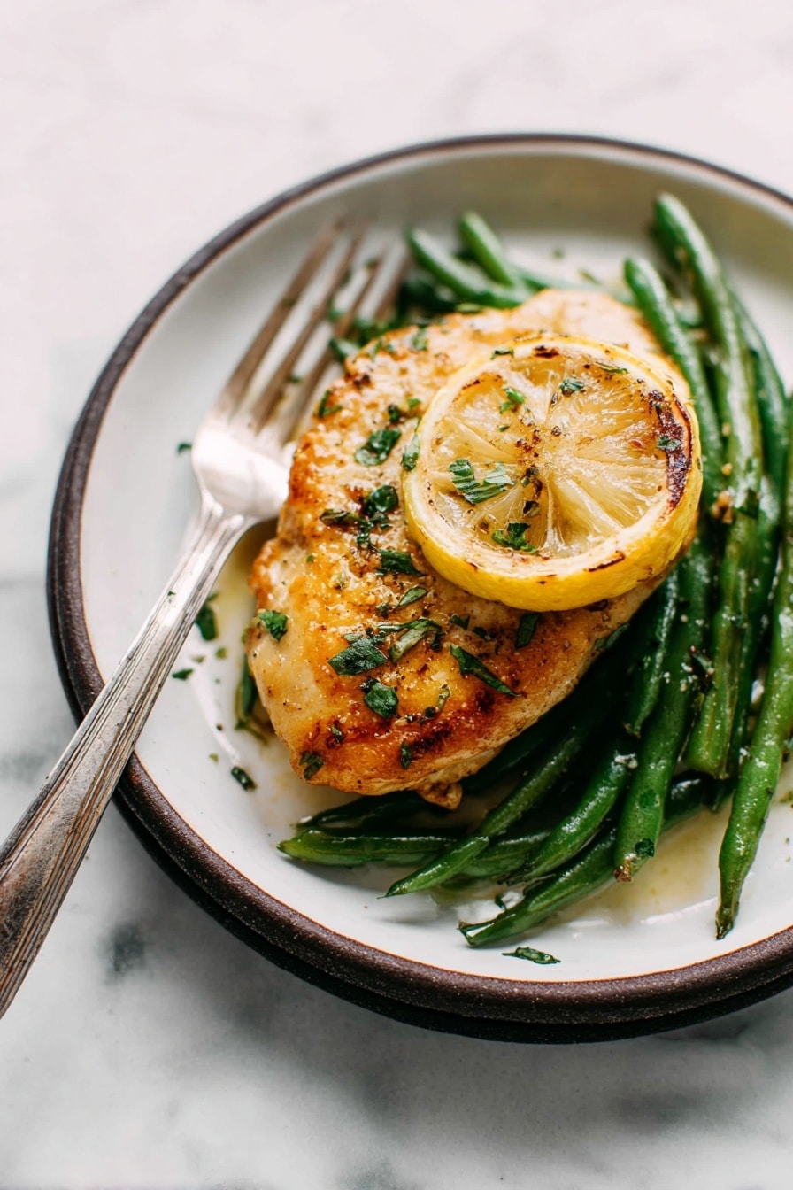 The image shows a single piece of golden-brown cooked chicken placed on top of a bed of green beans. Under the chicken, there is a slice of grilled lemon adding a pop of yellow color. The chicken is sprinkled with fresh green herbs and some seasoning that gives it a slightly glossy texture. The dish is served on a white plate with a dark rim, and a silver fork with an aged handle is resting on the edge of the plate. The surface beneath the plate has a white marbled texture, creating a clean and simple background. photo taken with an iphone --ar 2:3 --v 7 - Garlic Lemon Butter Chicken Skillet, Lemon Butter Chicken, Crispy Parmesan Chicken, Easy Chicken Skillet Dinner, Weeknight Chicken Recipes