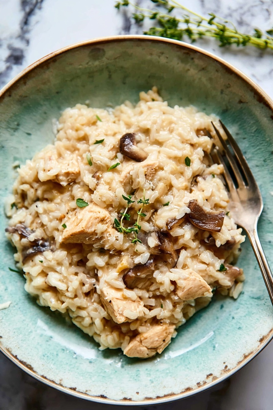 A textured turquoise bowl filled with creamy light beige risotto as the base layer, mixed with medium brown whole mushrooms and light tan chunks of chicken scattered evenly on top. A few sprigs of fresh green herbs sit on one side, adding a pop of color. The bowl rests on a white marbled surface with a folded dark grey cloth nearby, and a silver fork placed inside the bowl on the right side. The overall look is soft and earthy, with natural lighting enhancing the creamy texture of the dish photo taken with an iphone --ar 2:3 --v 7 - Creamy Chicken Mushroom Risotto, Chicken Mushroom Risotto, Easy Risotto Recipes, Comfort Food Dinner, Creamy Risotto