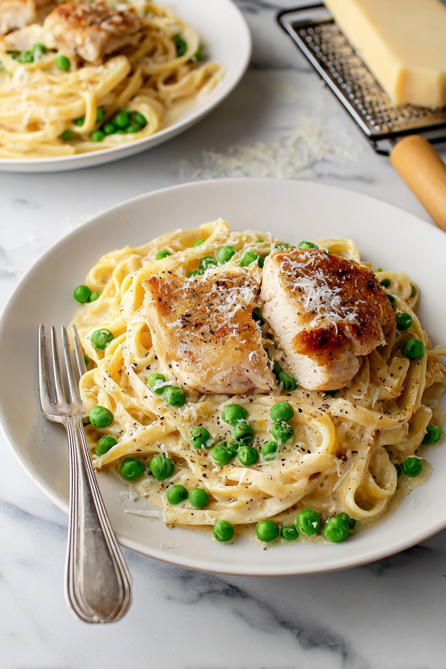 A white plate holds a creamy pasta dish with three slices of golden-brown grilled chicken placed on top. The pasta is mixed with bright green peas and coated in a smooth white sauce. Sprinkled parmesan cheese and black pepper garnish the dish. A spoon and fork rest on the left side of the plate. The plate sits on a white marbled surface, with a beige cloth napkin visible on the right side and a small piece of grated cheese and a grater partially seen toward the top right corner. photo taken with an iphone --ar 2:3 --v 7 - Turkey Alfredo Pasta, creamy turkey pasta, easy Alfredo pasta, leftover turkey recipes, cheesy pasta dinner