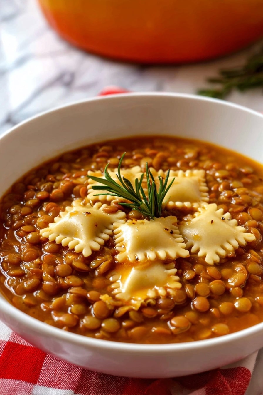 The image shows a white bowl filled with a thick vegetarian lentil soup layered with small, round brown lentils covering the entire surface, mixed with several square pieces of pale yellow pasta scattered evenly on top. The soup has a rich, brownish-orange broth giving the dish a warm color, with a small green rosemary sprig placed in the center as a garnish. The bowl rests on a red and white checkered cloth with a white marbled surface below, and a blurred background hinting at an orange pot. Photo taken with an iphone --ar 2:3 --v 7 - Umbrian Lentil Soup with Pasta, Italian Lentil Soup, hearty vegetarian soup, traditional Italian lentil recipes, easy warm Italian soup