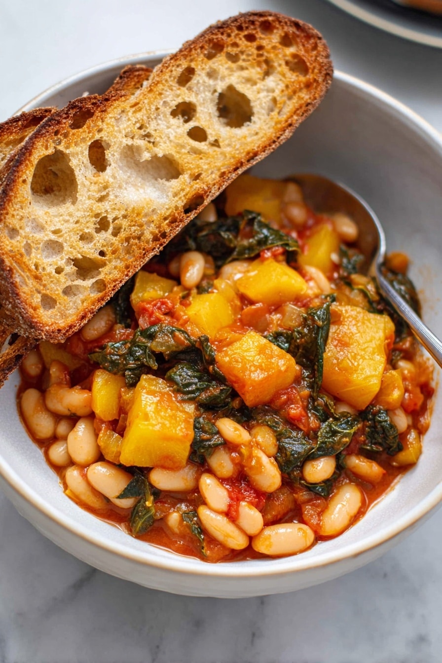 A white bowl filled with two thick slices of toasted bread resting on the left side, showing their golden-brown crispy texture with some holes and rough edges. The main part of the bowl is filled with a colorful mix of cooked white beans, yellow chunks of squash, and dark green leafy vegetables, all coated in a rich, slightly shiny red-orange sauce. The ingredients are close together, showing a hearty, rustic stew. A silver spoon is partially visible on the right side of the bowl, touching the food. The bowl sits on a white marbled surface. photo taken with an iphone --ar 2:3 --v 7 - Stewed Great Northern Beans with Kale, Tomatoes, and Herbs, hearty bean and kale stew, healthy vegetarian dinner, wholesome bean recipes, easy bean and greens dish
