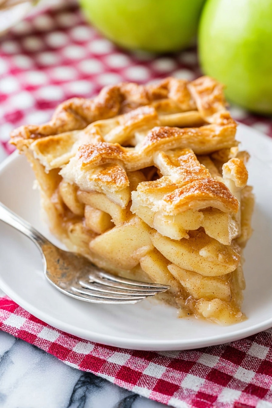 A piece of apple pie sits on a white plate with a silver fork resting beside it. The pie has a golden-brown lattice crust on top, with visible layers of soft, spiced apple slices underneath that appear juicy and tender. The crust edges are slightly crimped and have a flaky texture. Behind the pie, there are two green apples slightly out of focus. The plate is placed on a red and white checkered cloth, all set on a white marbled surface. Photo taken with an iphone --ar 2:3 --v 7 - The BEST Apple Pie, apple pie recipe, homemade apple pie, flaky apple pie crust, easy apple pie dessert