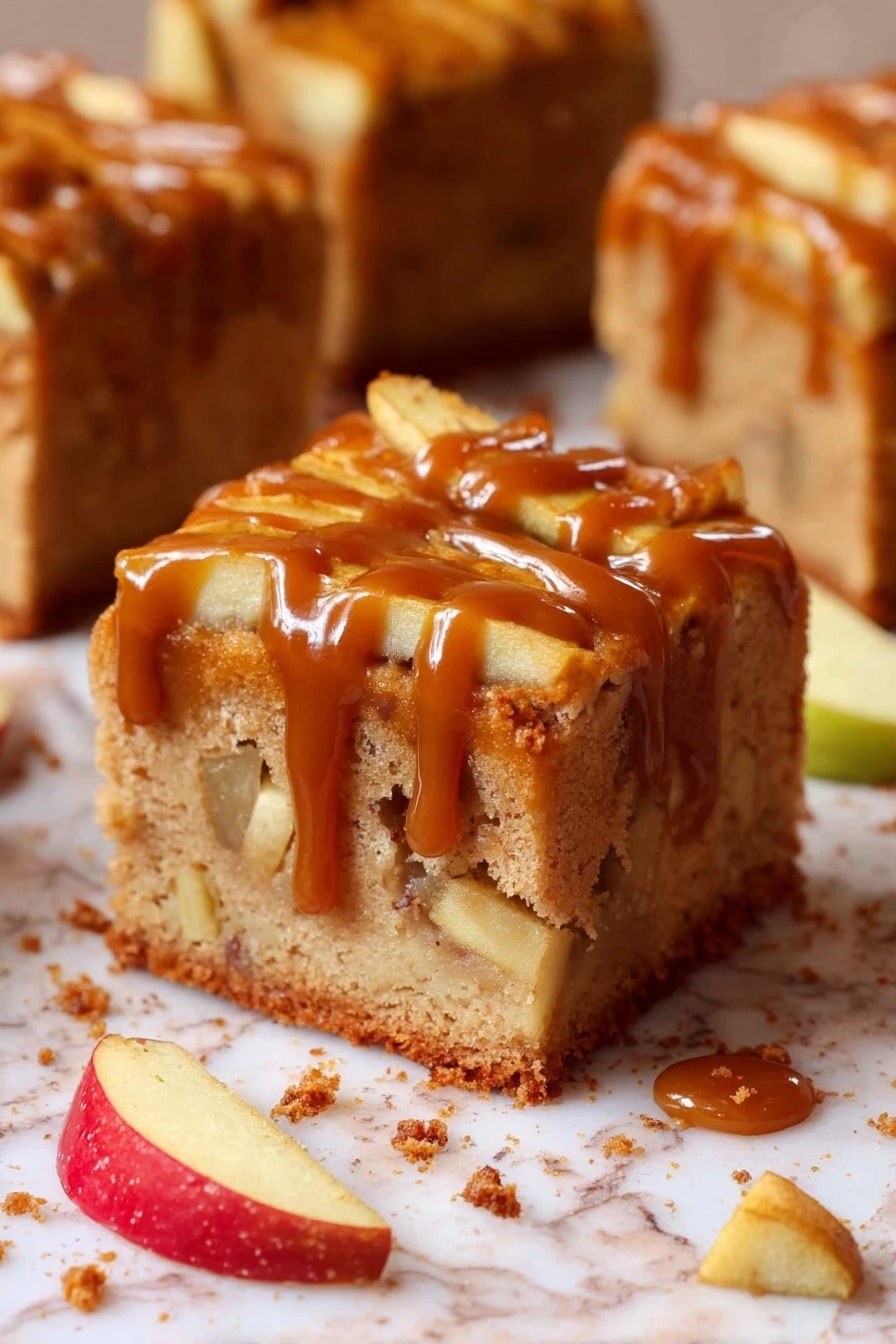 A thick square slice of apple cake shows two visible layers: the bottom is a light brown soft cake base with apple chunks inside, and the top layer is covered with thin apple slices partially lengthened by a messy layer of glossy caramel sauce dripping down the sides. The cake sits on white marbled surface sprinkled with crumbs, small apple chunks, and thin apple slices nearby. The background shows more similar cake slices out of focus. Photo taken with an iphone --ar 2:3 --v 7 - Caramel Apple Cake, apple cake with caramel, fall apple dessert, moist apple cake recipe, easy apple cake with caramel drizzle