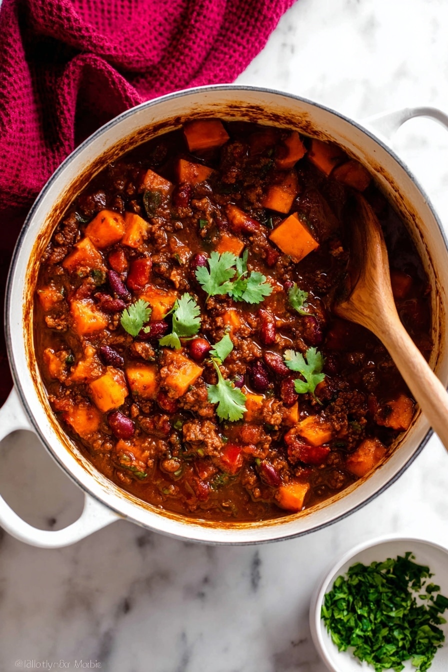 A white pot filled with thick stew that has three main layers: a dark brown sauce base, chunky orange sweet potato pieces, and visible red and brown beans mixed with ground meat; a few green cilantro leaves float on top near the center for color contrast. A wooden spoon is partially dipped on the right side, stirring the stew, showing the dense texture and rich sauce coating all ingredients. The pot rests on a white marbled surface with a dark red cloth draped in the upper left corner and a small white bowl filled with chopped green herbs placed near the bottom right. Photo taken with an iphone --ar 2:3 --v 7 - Vegetarian Pumpkin Chili, Healthy Pumpkin Chili, Cozy Vegetarian Dinner, Fall Vegetarian Recipes, Hearty Pumpkin Chili