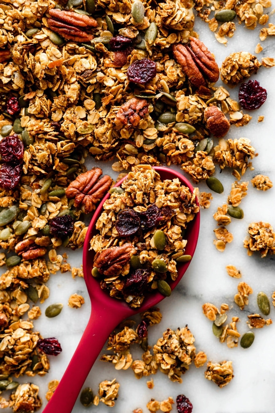 The image shows a close-up of crunchy granola scattered on a white marbled surface with a red spoon filled with granola placed near the center. The granola is made of golden-brown toasted oat clusters mixed with darker brown pecans, green pumpkin seeds, and dark red dried cranberries. The textures vary from rough and chunky oats and nuts to smooth seeds, creating a rich and inviting look. The red spoon contrasts strongly with the white background and the natural colors of the granola around it. photo taken with an iphone --ar 2:3 --v 7 - Crunchy Pumpkin Spice Granola, Pumpkin Spice Granola, Fall Breakfast Ideas, Healthy Pumpkin Granola, Cozy Autumn Snacks