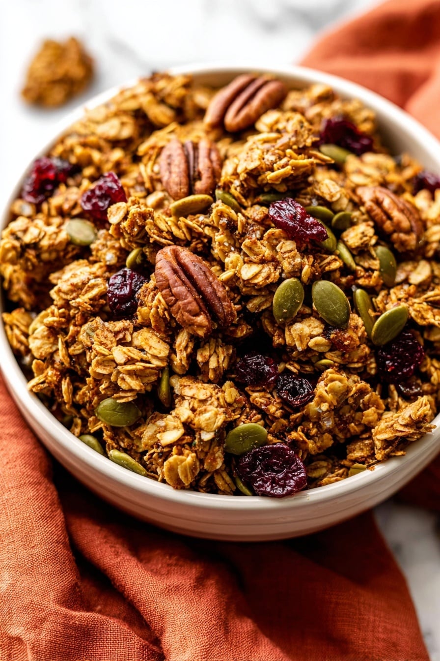 A close-up view of a white bowl filled with chunky granola clusters that have a golden-brown color and rough texture, mixed with whole pecans that are dark brown and ridged, green pumpkin seeds scattered throughout, and small pieces of deep red dried cranberries. The bowl is placed on top of a folded burnt orange cloth on a white marbled surface. photo taken with an iphone --ar 2:3 --v 7 - Crunchy Pumpkin Spice Granola, Pumpkin Spice Granola, Fall Breakfast Ideas, Healthy Pumpkin Granola, Cozy Autumn Snacks